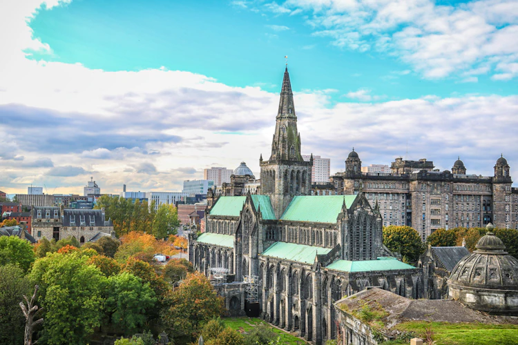 Smukt overblik over Glasgow Cathedral med gotisk spir og grønne kobbertage omgivet af efterårsfarver og Glasgow skyline i Skotland