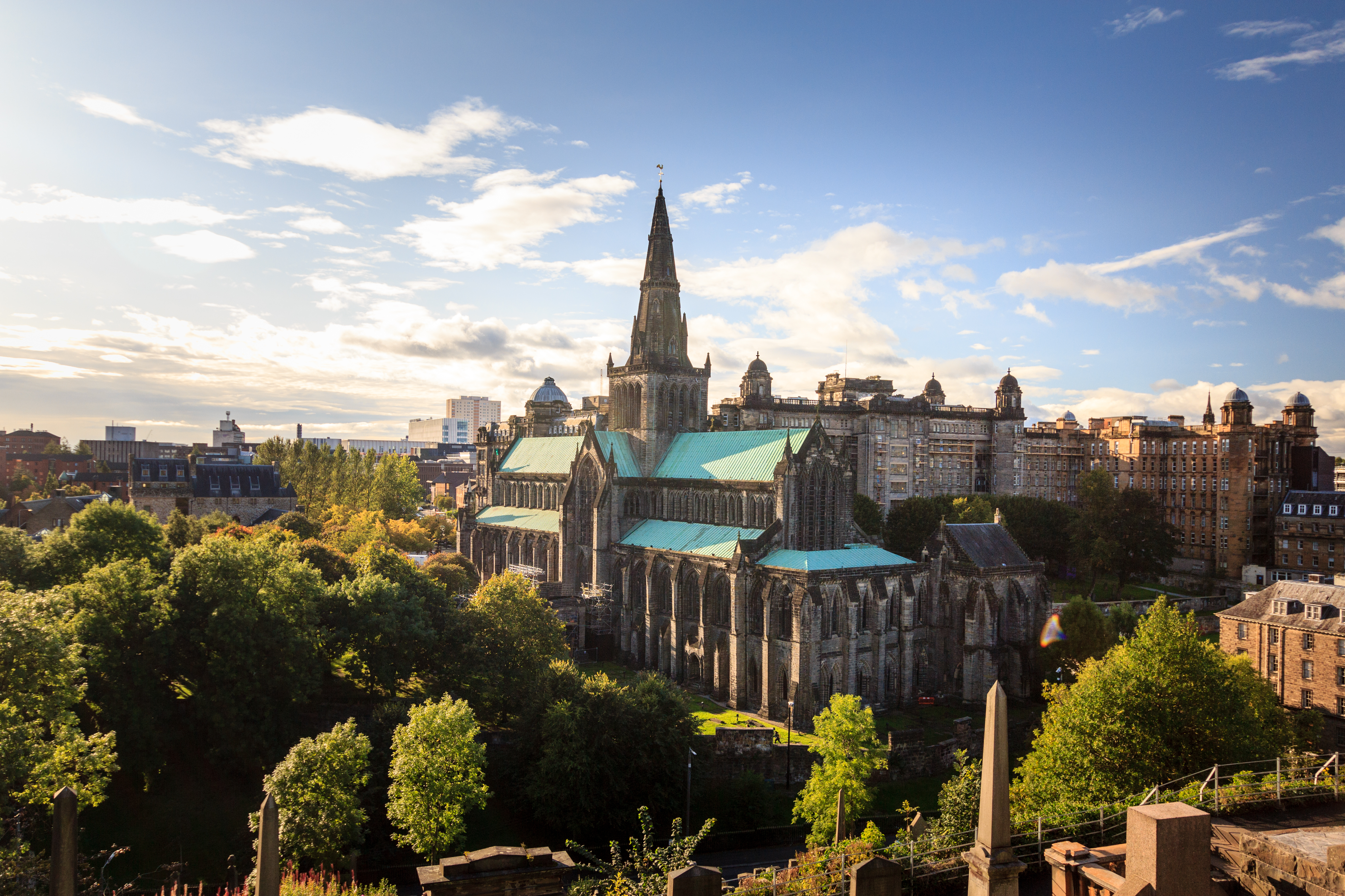 Udsigt over den imponerende Glasgow katedral med gotisk spir og grønt kobbertag omgivet af skovklædte omgivelser i hjertet af Glasgow