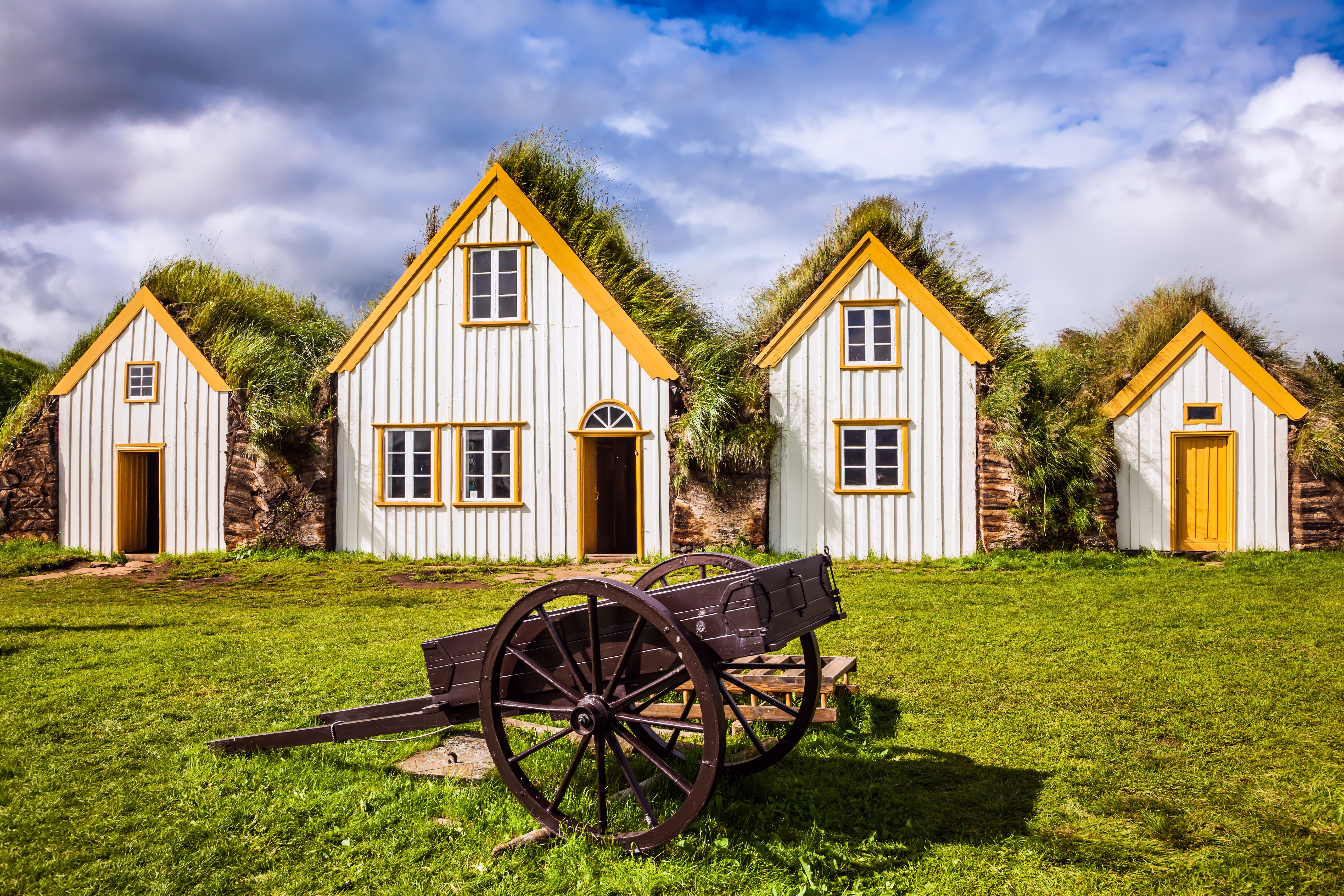 Maleriske traditionelle torvhuse på Glaumbaer museum i Island med grønne græstage og hvide facader med gule vinduesrammer på en smuk sommerdag