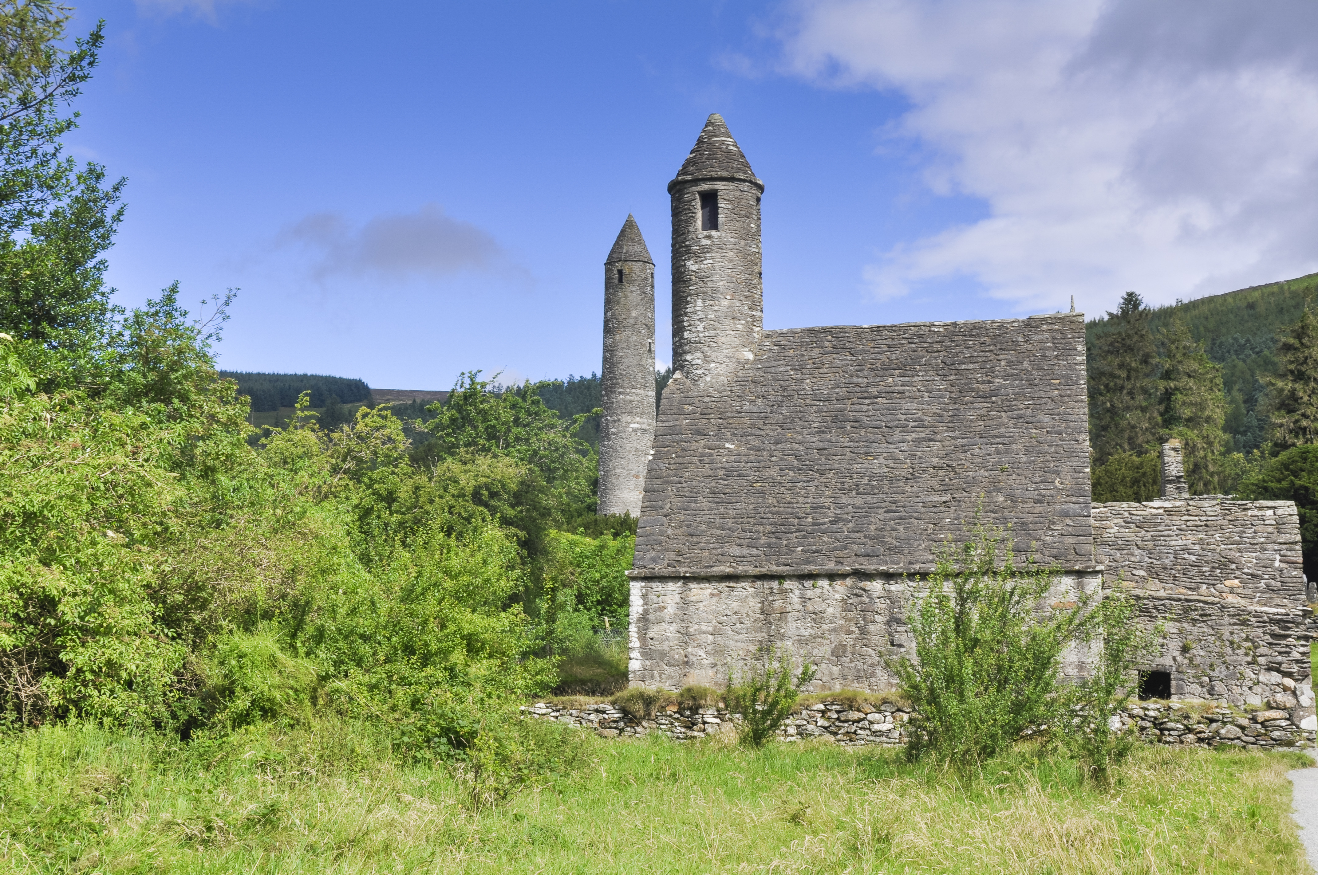 Historiske klosterruiner ved Glendalough i Irland med det ikoniske keltiske rundtårn og St. Kevins Kitchen fra det 6. århundrede i naturskønne omgivelser