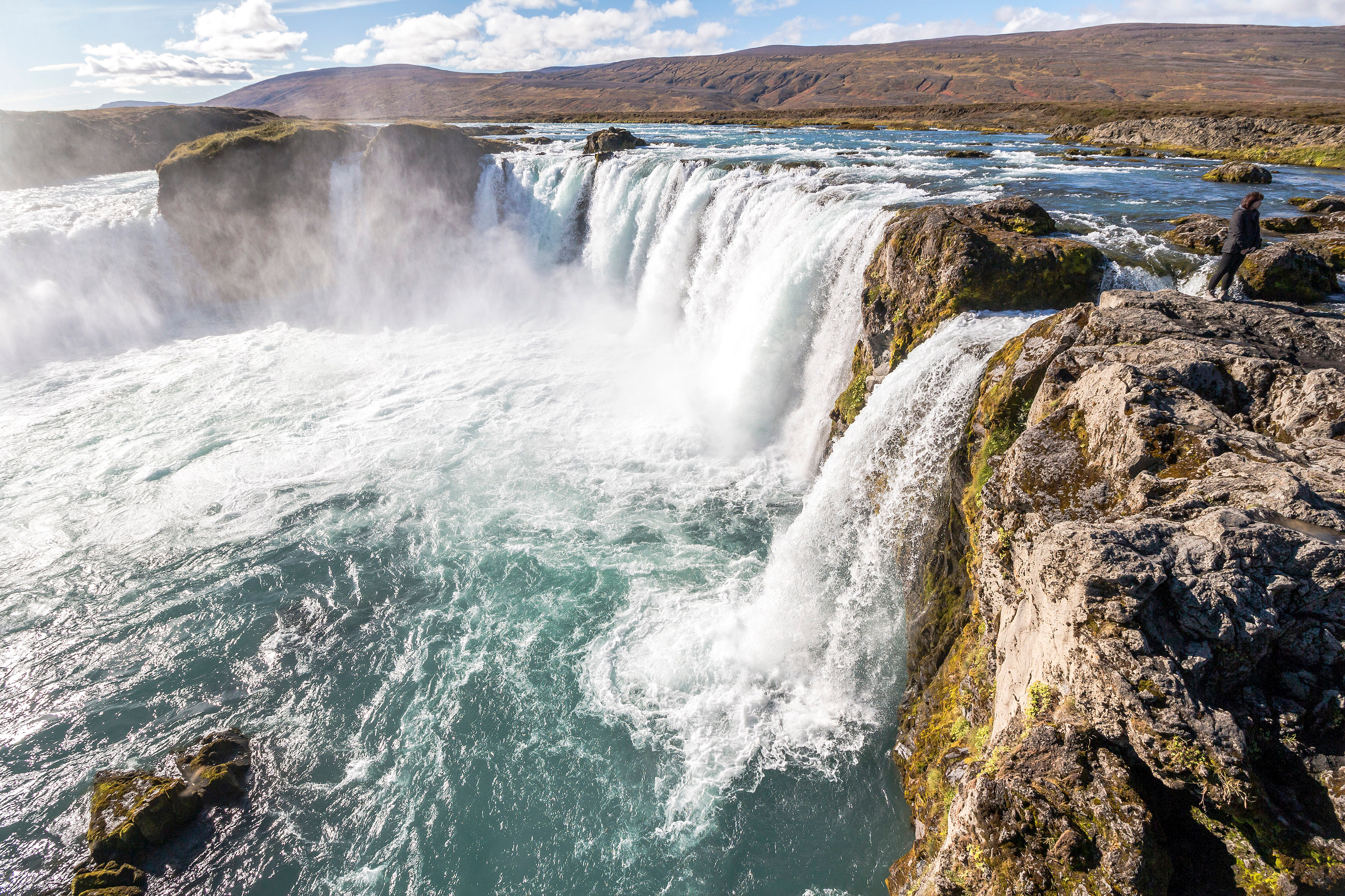 Smukt udsigt over det berømte Godafoss vandfald på Island med turkisblåt vand der fosser over sorte vulkanklipper under en delvis skyet himmel