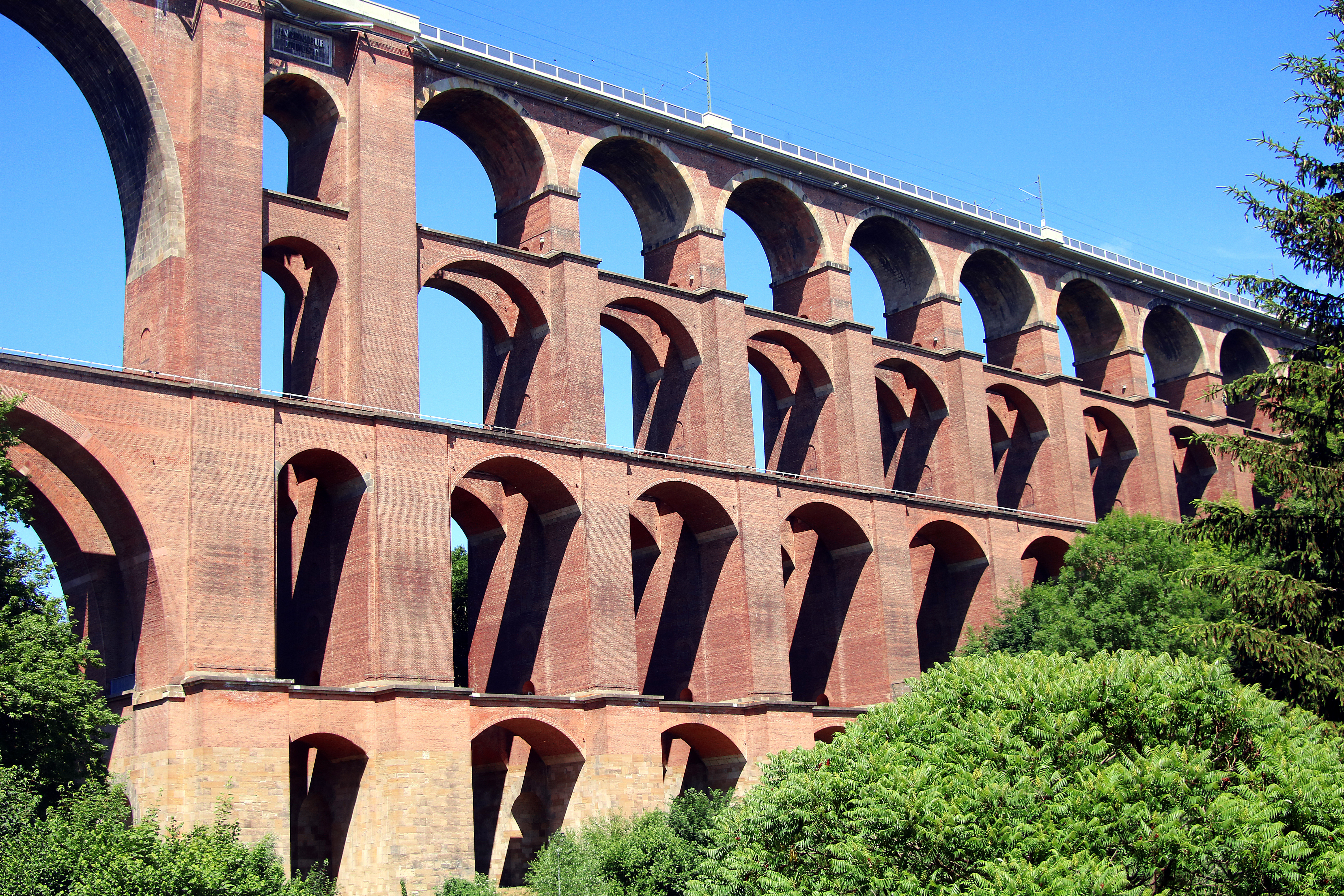 Storslået udsigt til Goeltzschtalbruecke i Sachsen, Tyskland - en historisk murstensbroer med tre etager af røde buer omgivet af frodig grøn natur