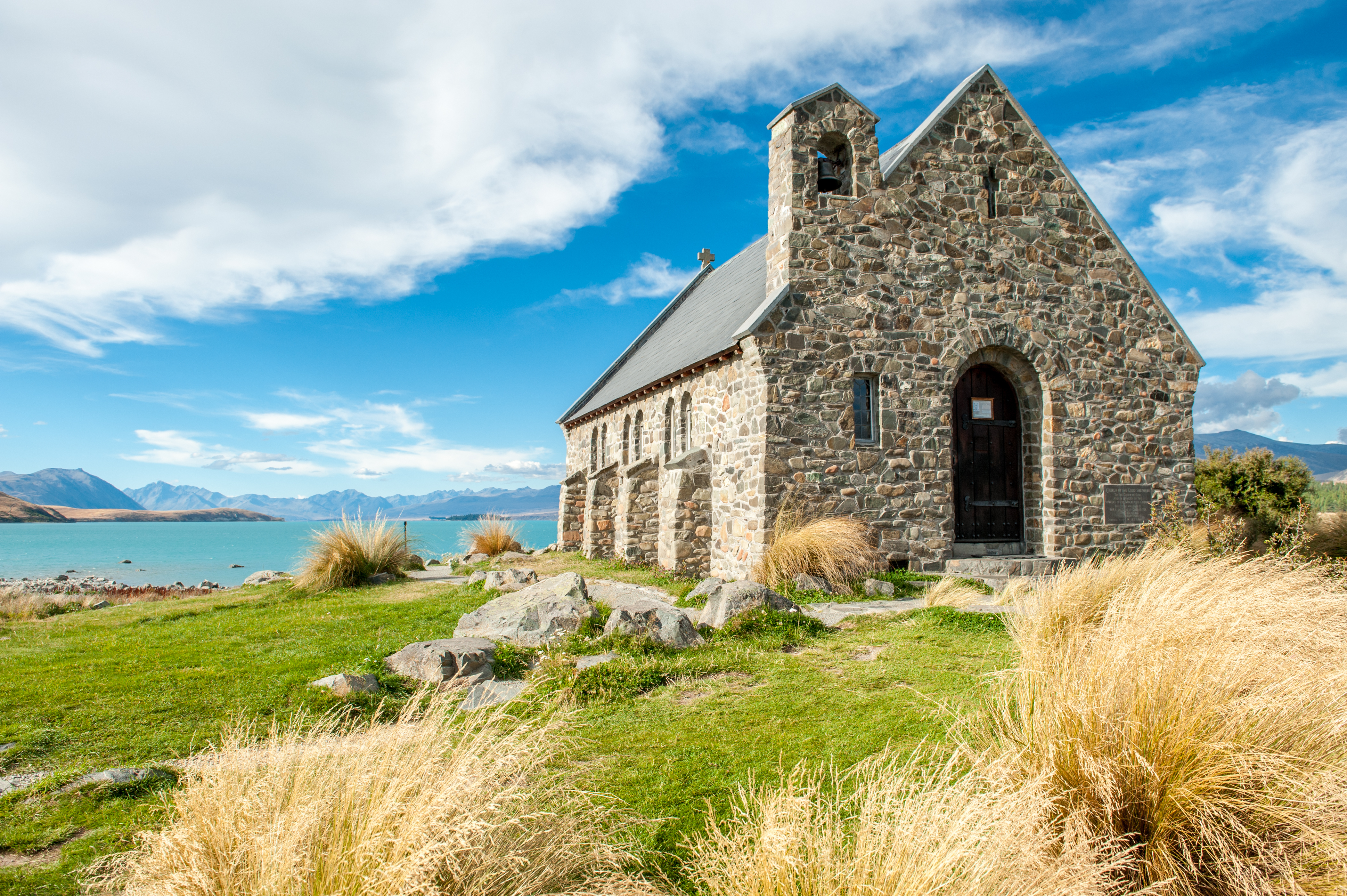Den smukke stenkirke Church of the Good Shepherd ved det turkisblå Lake Tekapo i New Zealand med gyldent tussockgræs i forgrunden
