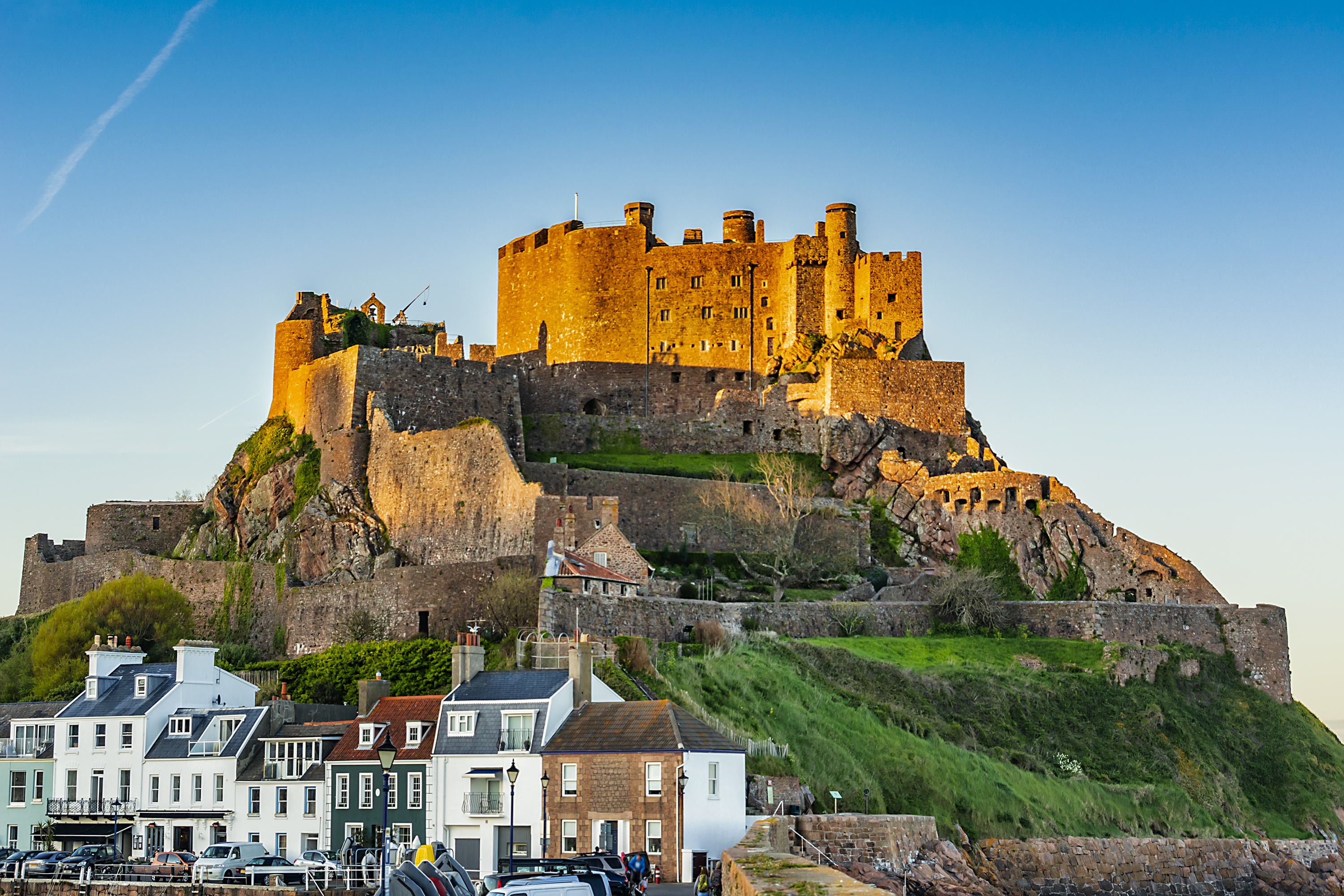Mont Orgueil Slot i Gorey på Jersey badet i varmt solnedgangslys, med historiske fæstningsmure og hvide huse ved havnen