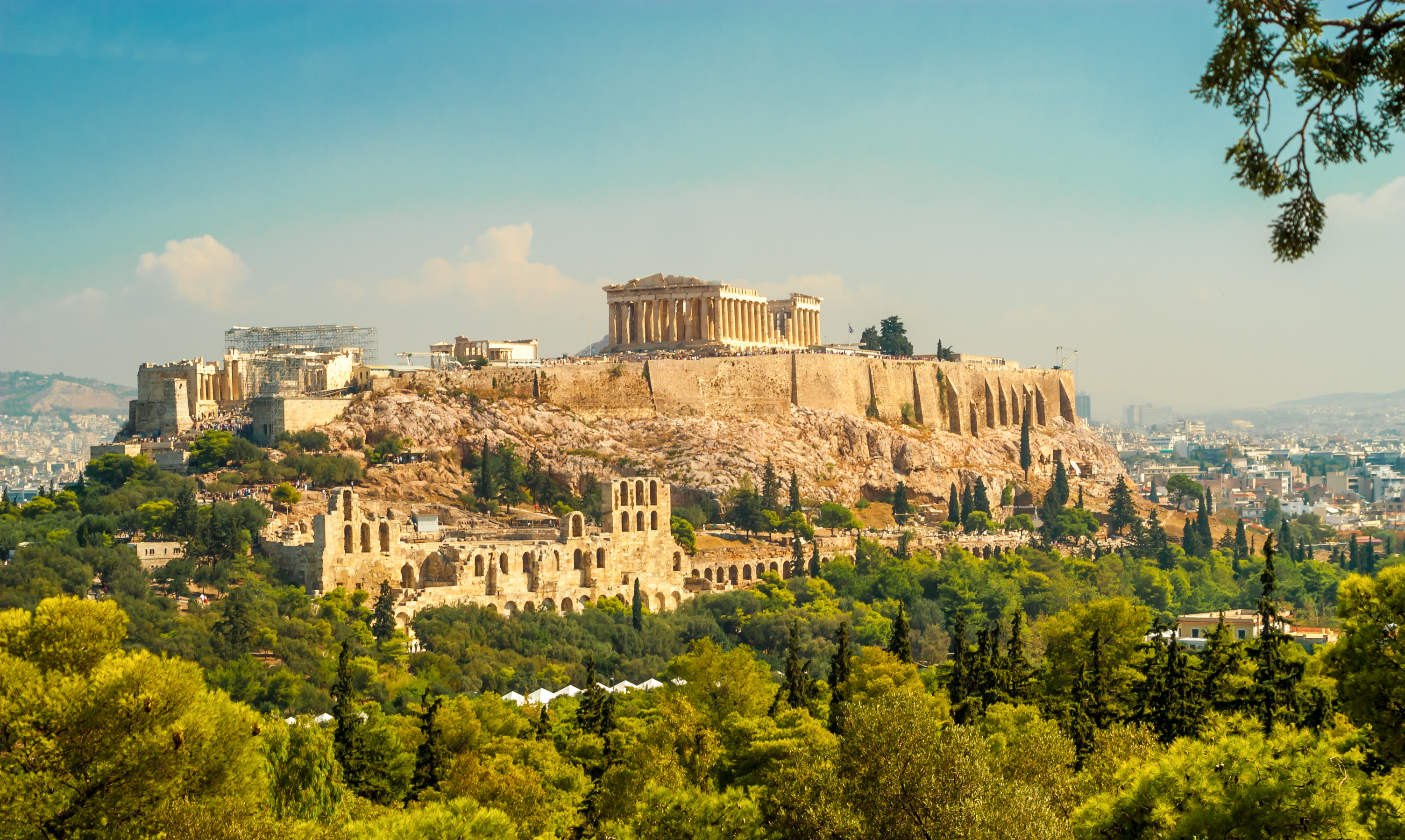 Akropolis-ruinerne på klippen med udsigt over det moderne Athen omgivet af grønne træer