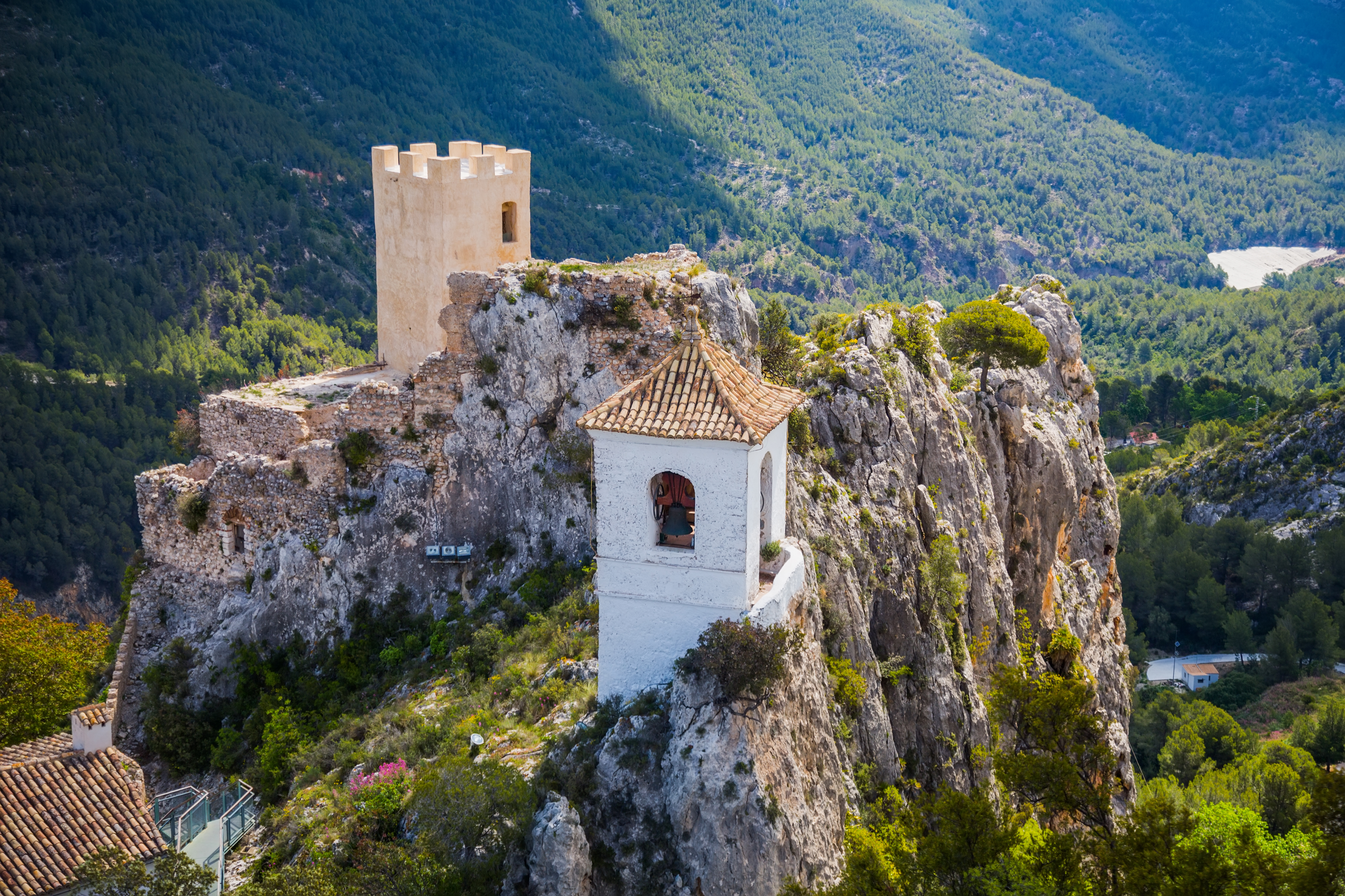 Guadalest med ikonisk hvidt klokketårn og gammel fæstningstårn på høj klippetop omgivet af frodig bjergvegetation i Spanien