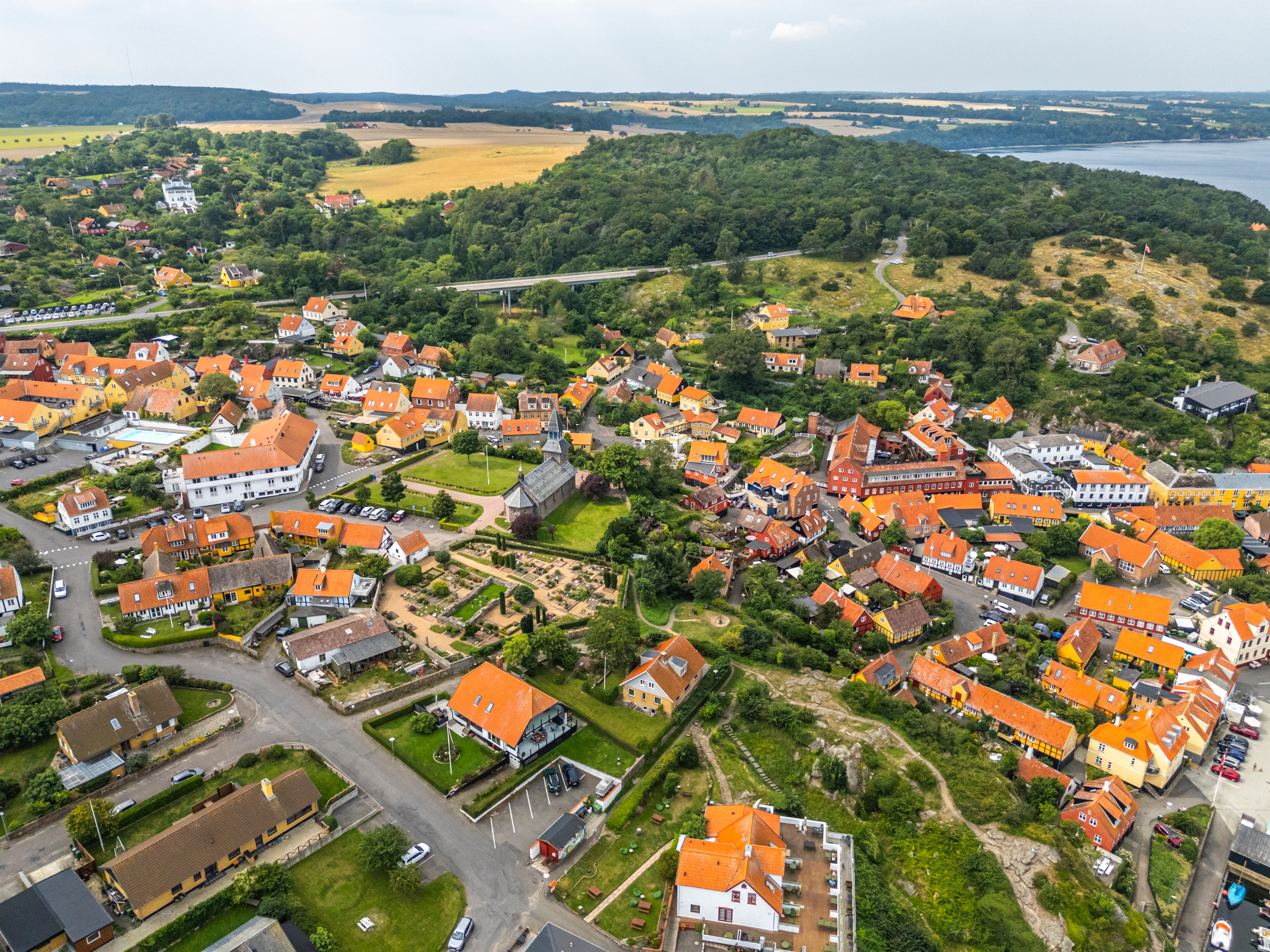 Panoramaudsigt over Gudhjem by på Bornholm om sommeren med røde tegltage og grønne skove ned mod Østersøen