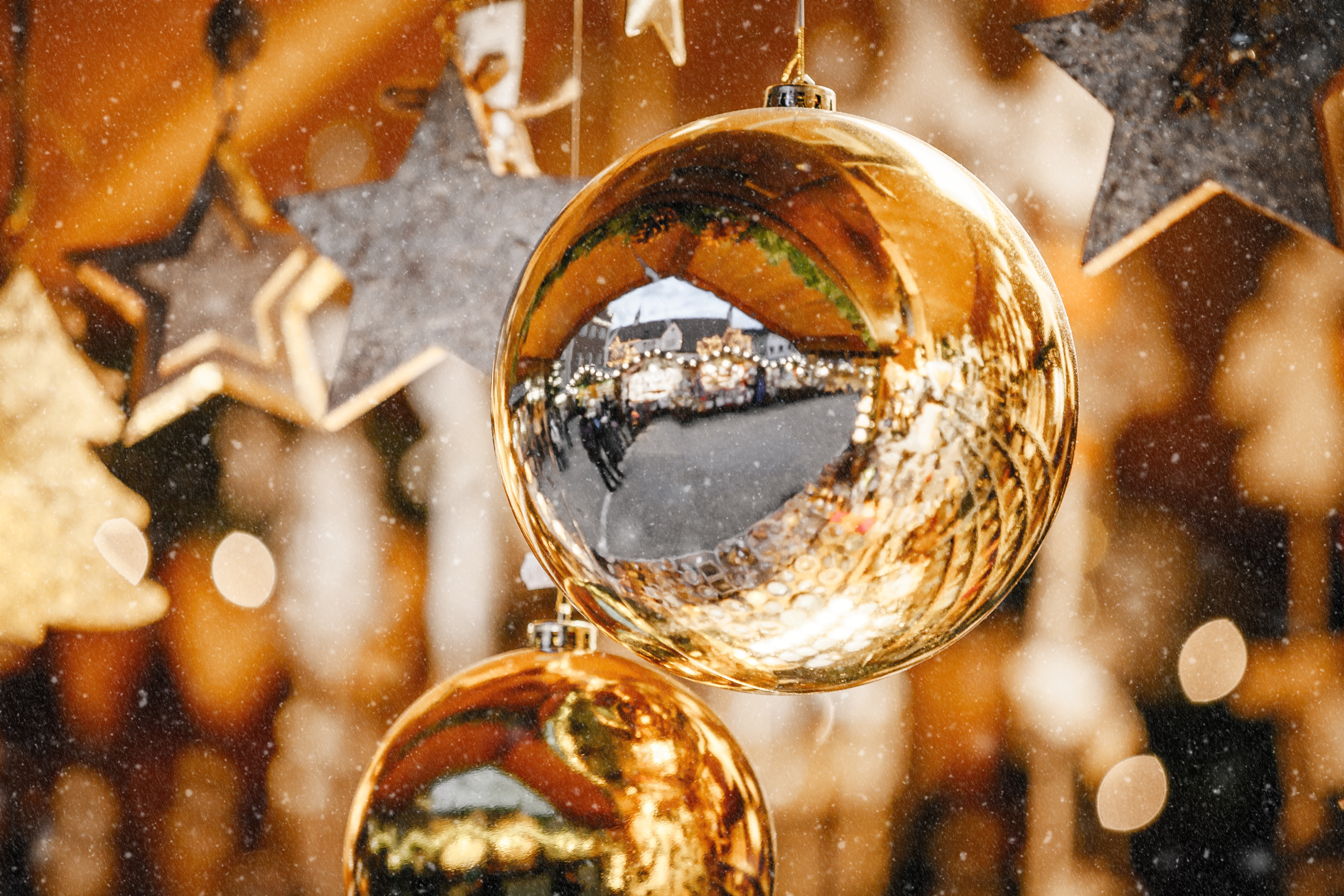 Nærbillede af gyldne julekugler der spejler julemarkedet i Trentino Alto Adige, Italien, med dekorative stjerner i baggrunden