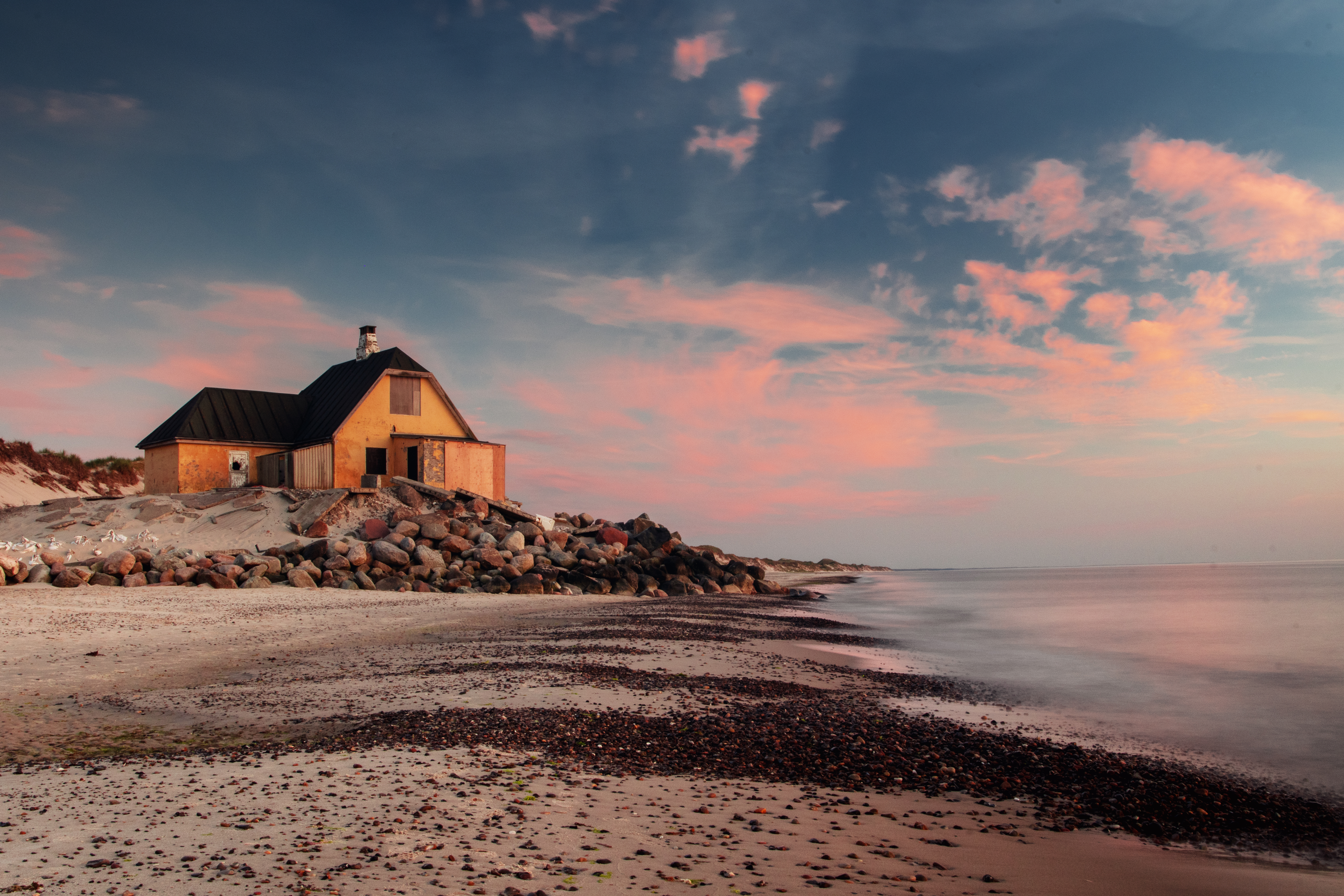 Charmerende gult træhus på Skagens kyst med dramatisk solnedgang over Skagerrak, der perfekt illustrerer den særlige nordiske kystidyl i Danmarks nordligste punkt