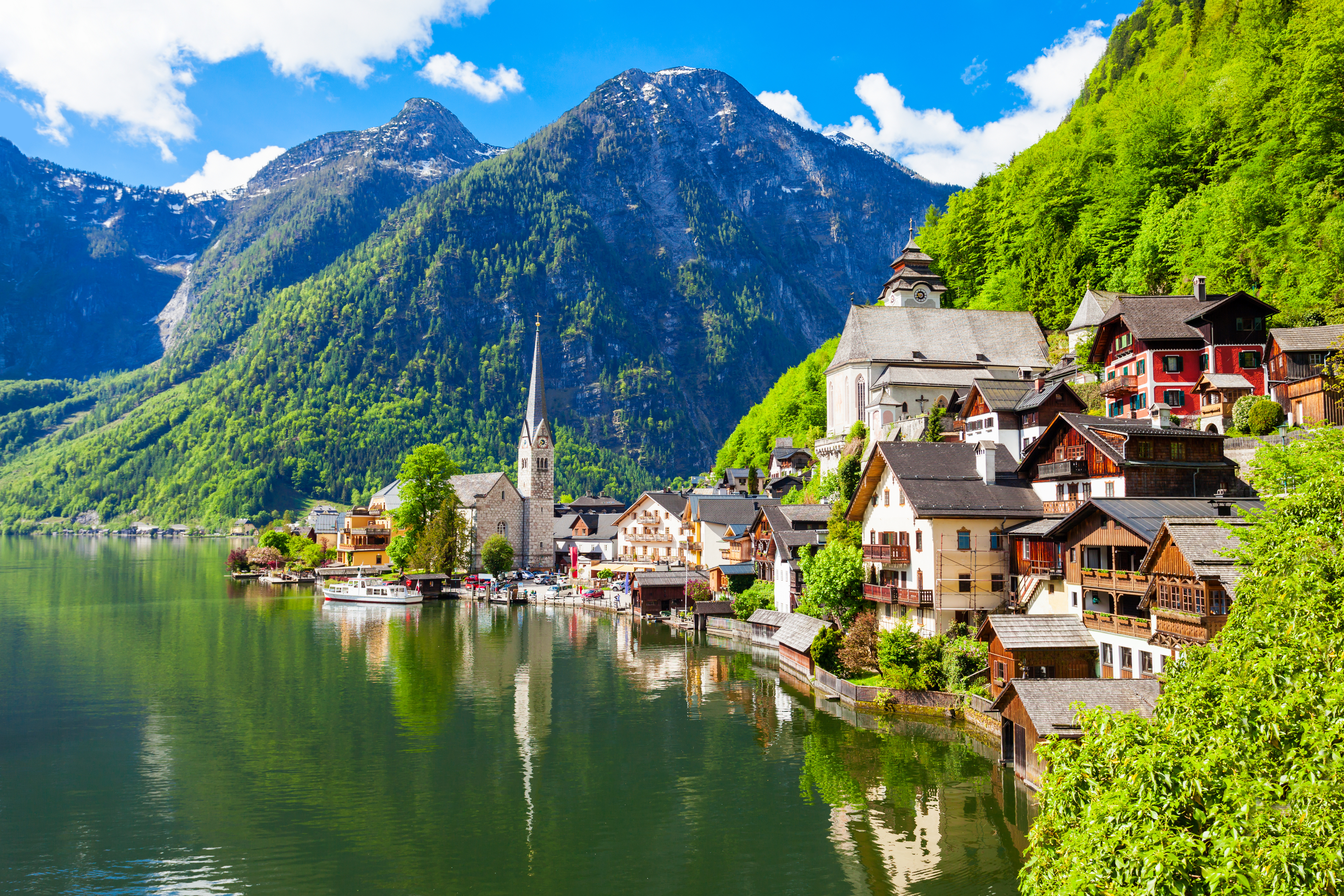 Det naturskønne Hallstatt med historiske bygninger og kirketårn reflekteret i den krystalklare alpesø omgivet af sneklædte bjerge