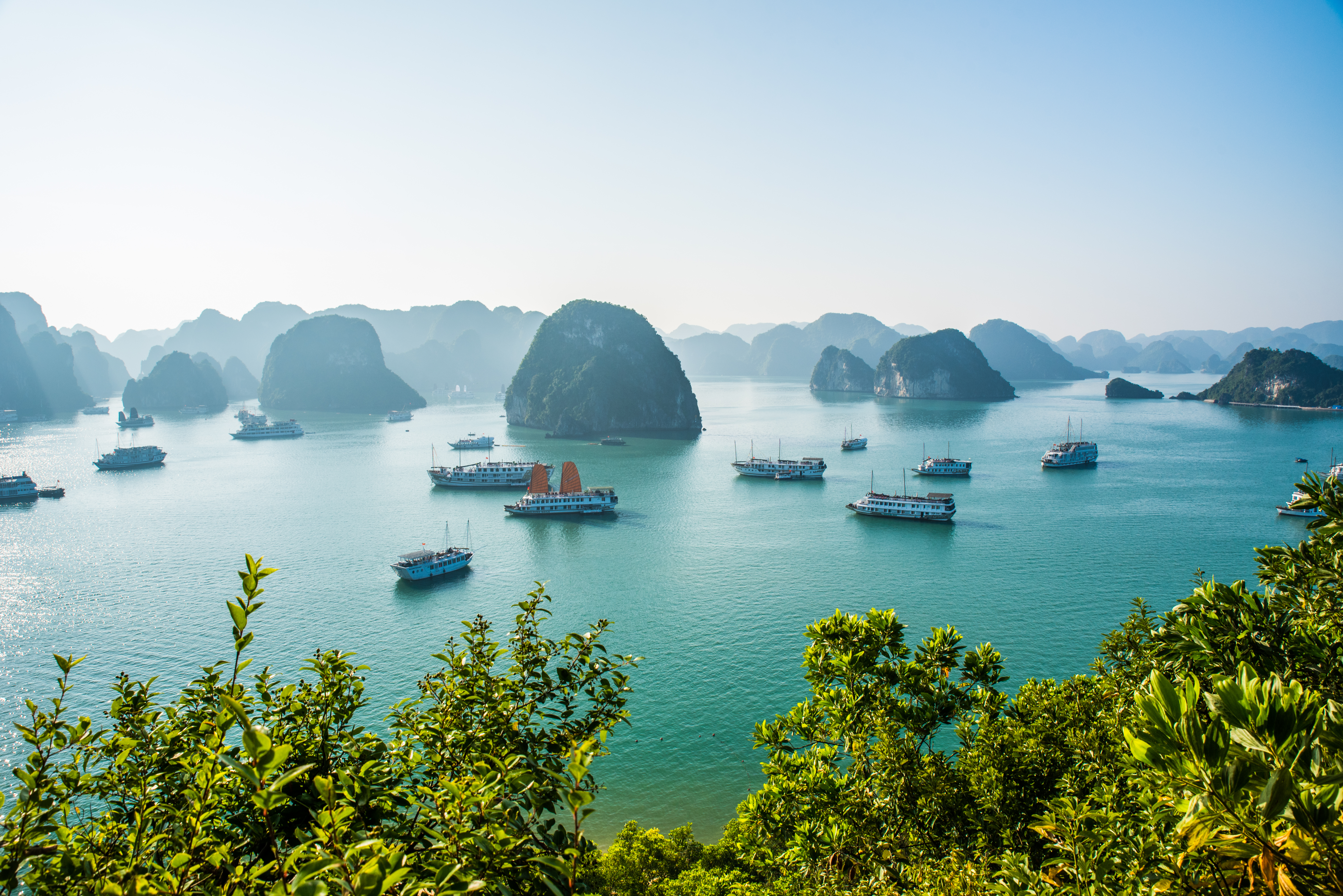 Udsigt over den verdensberømte Ha Long Bugt i Vietnam med turkisblåt hav, dramatiske kalkstensformationer og traditionelle junke-sejlbåde under blå himmel