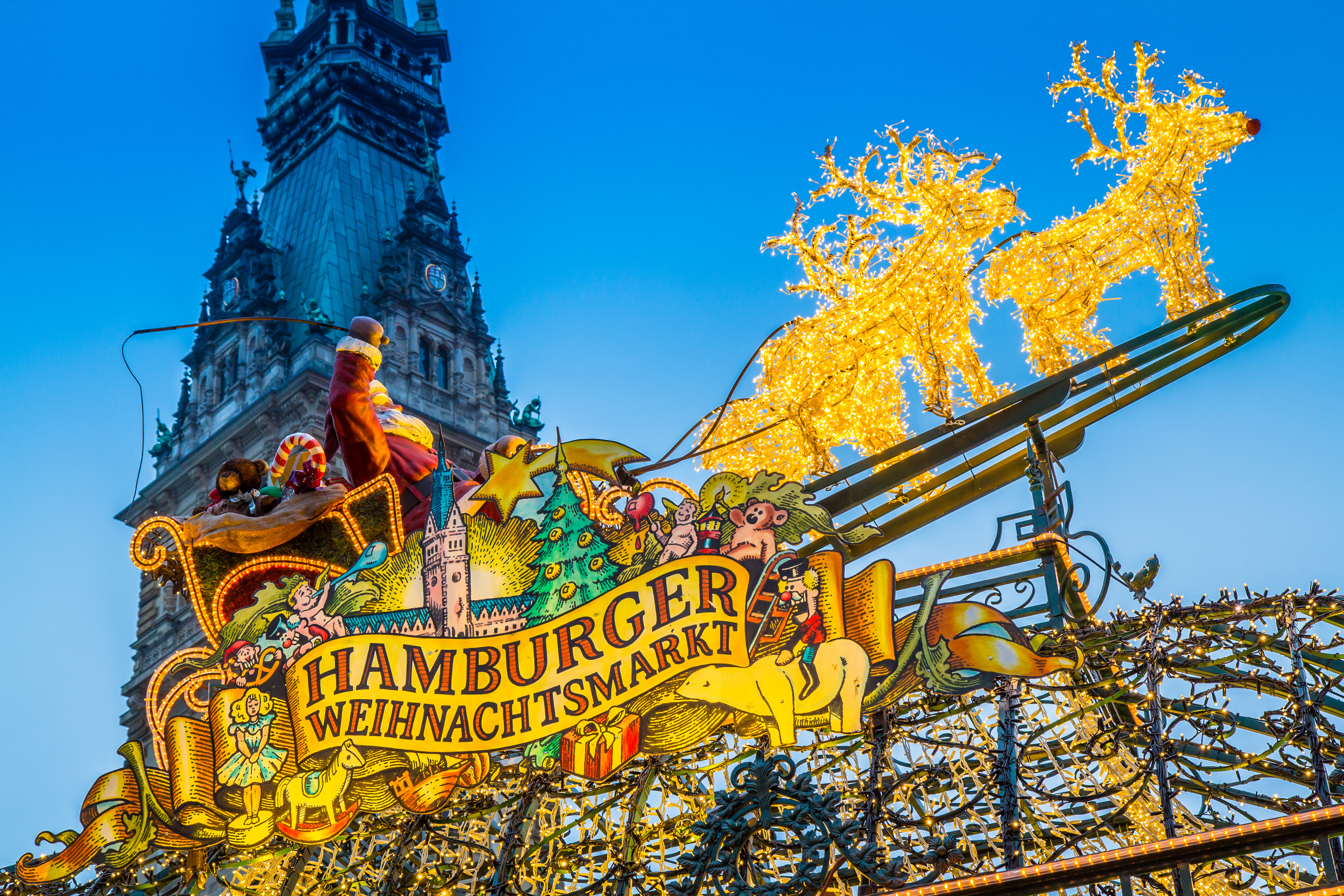 Indgangen til Hamburger Weihnachtsmarkt prydet med gyldne lysrensdyr og julemand i kane foran Hamburgs historiske rådhus