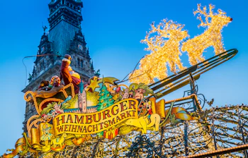 Indgangen til Hamburger Weihnachtsmarkt prydet med gyldne lysrensdyr og julemand i kane foran Hamburgs historiske rådhus