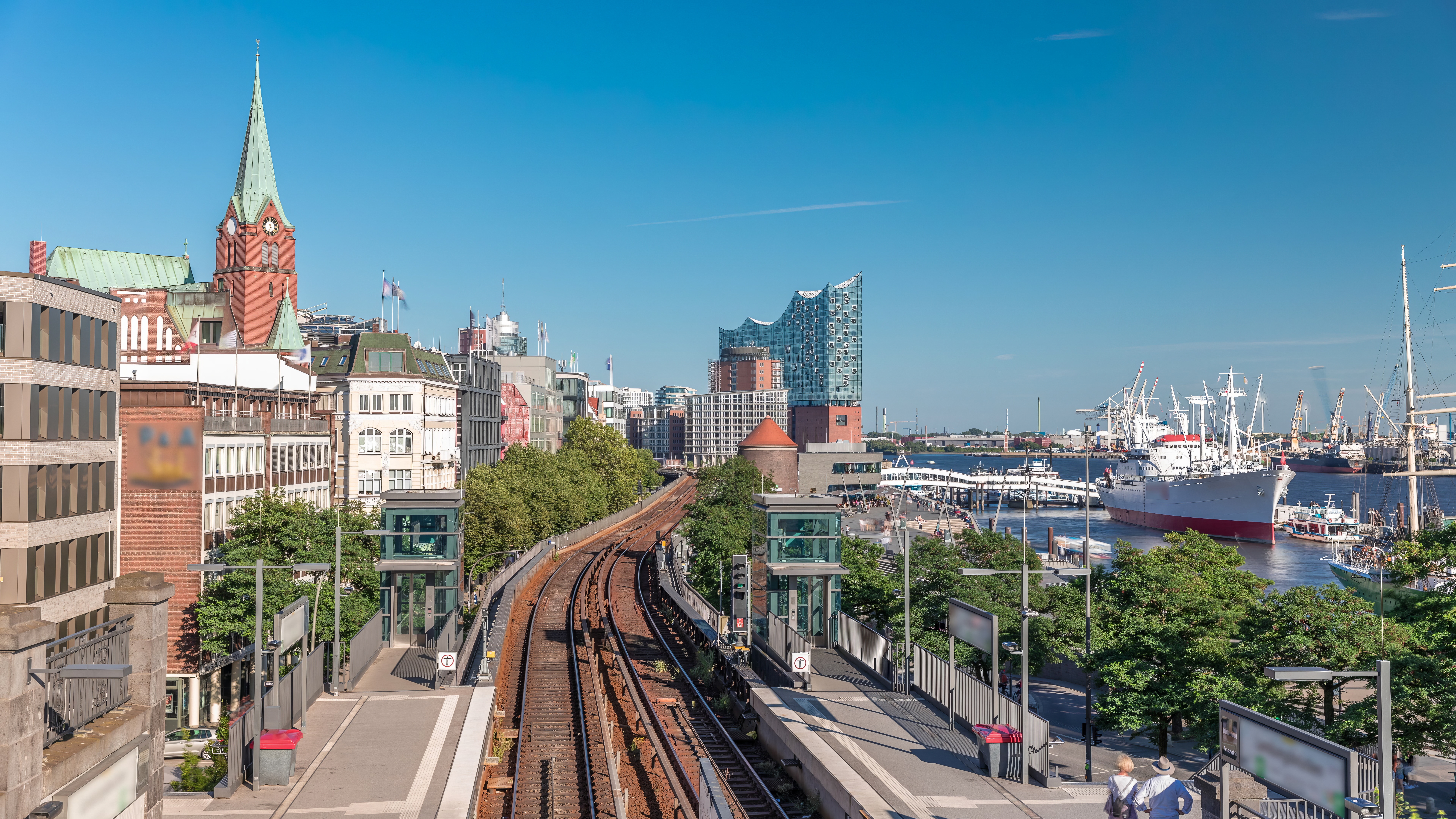 Panoramabillede af Hamburg med togstation ved Landungsbrücken, den ikoniske Elbphilharmonie og travl havnefront