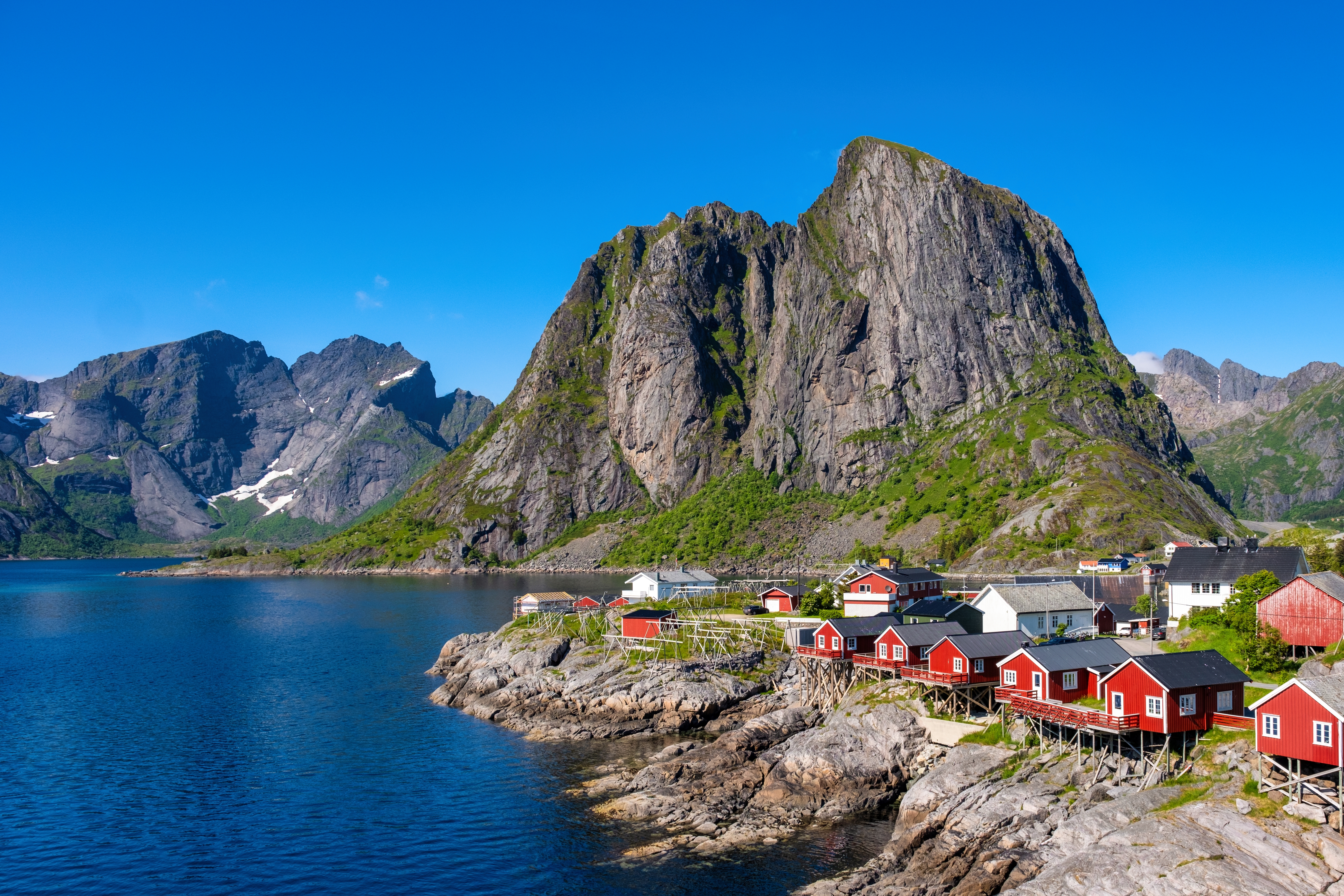 Smuk norsk kystby Hamnøy på Lofoten med traditionelle røde rorbu-hytter på klippekysten omgivet af høje fjelde og klart blåt fjordvand
