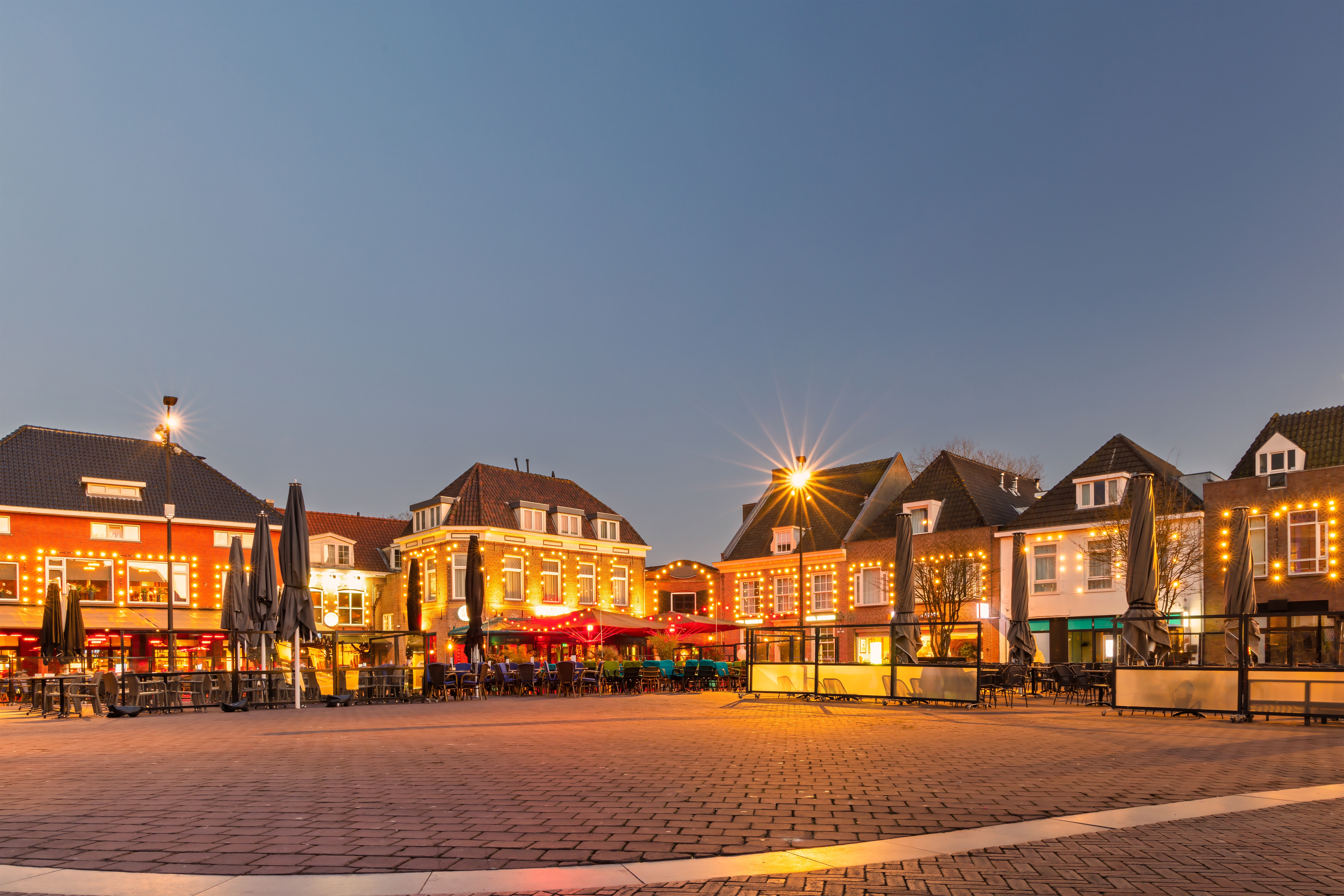Aftenstemning på det historiske torv i Harderwijk i Gelderland, Holland, med varmt oplyste caféer og restauranter langs klassiske hollandske handelsbygninger