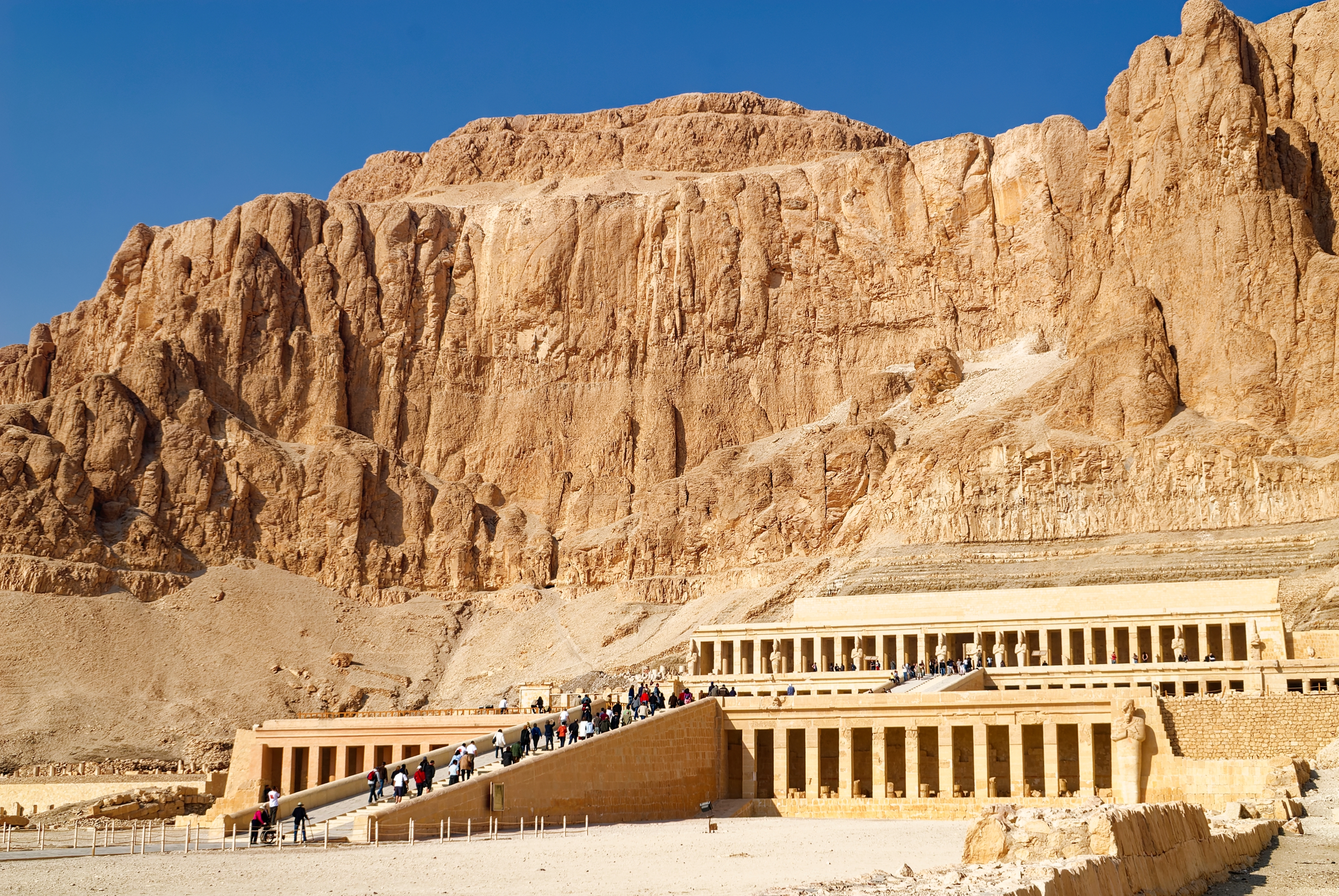 Det velbevarede Hatshepsut-tempel i Luxor ved Kongernes Dal i Egypten, med turister der går op ad ramperne til de antikke søjlegange