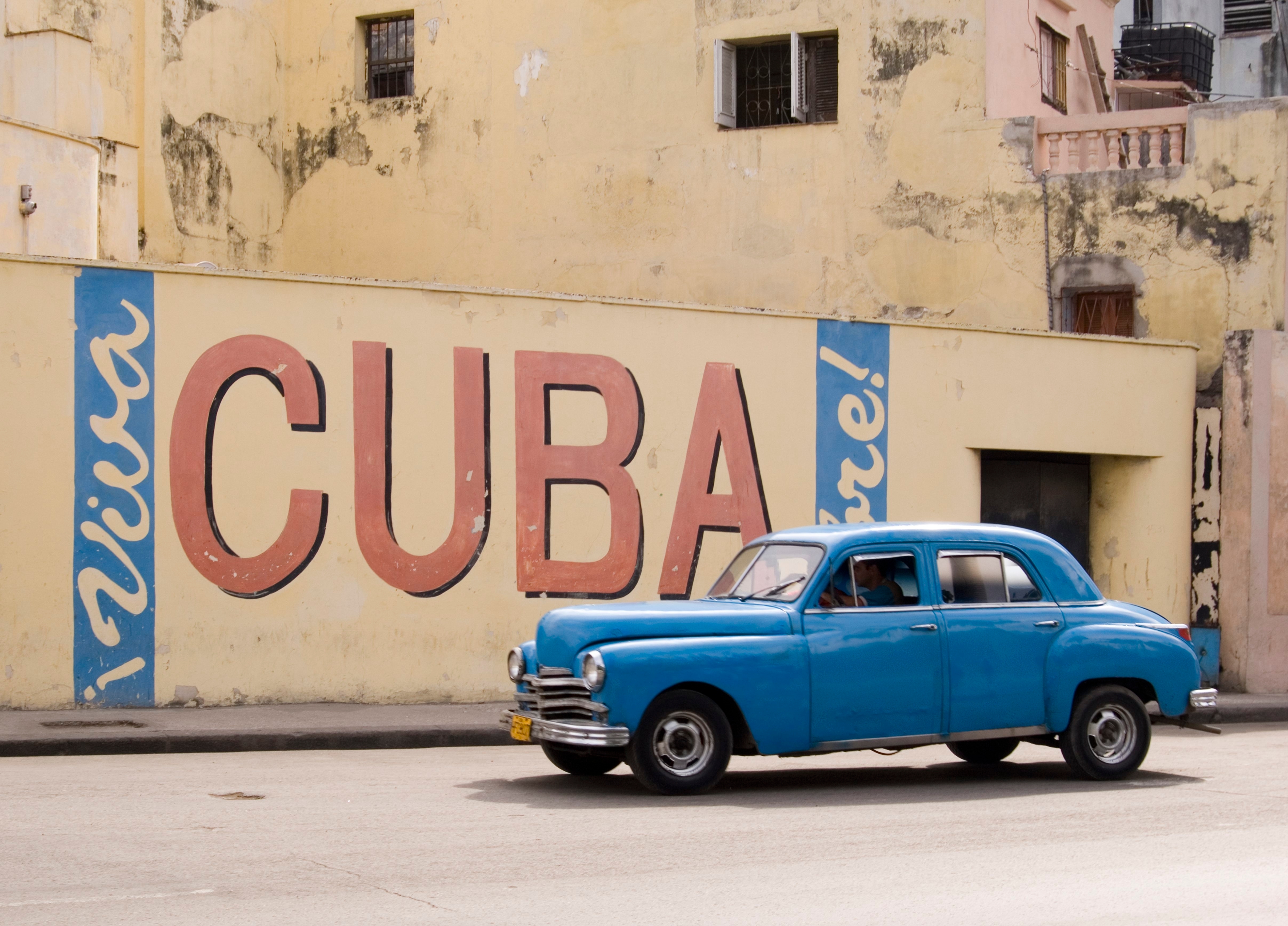 Blå oldtimer bil på gade i Havana med Cuba vægmaleri