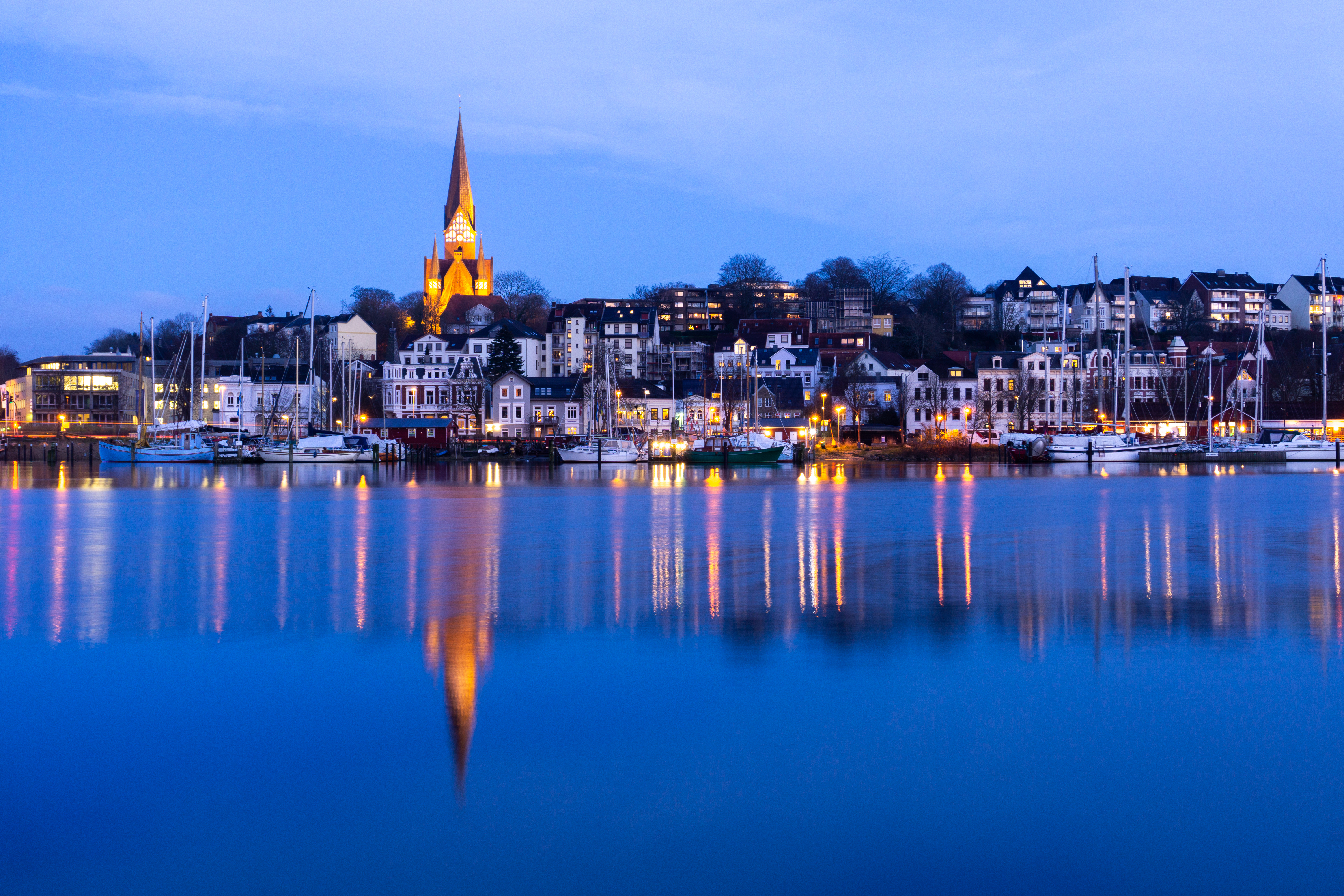 Idyllisk havneby ved aftentid med historisk kirke og marina med sejlbåde under blå himmel