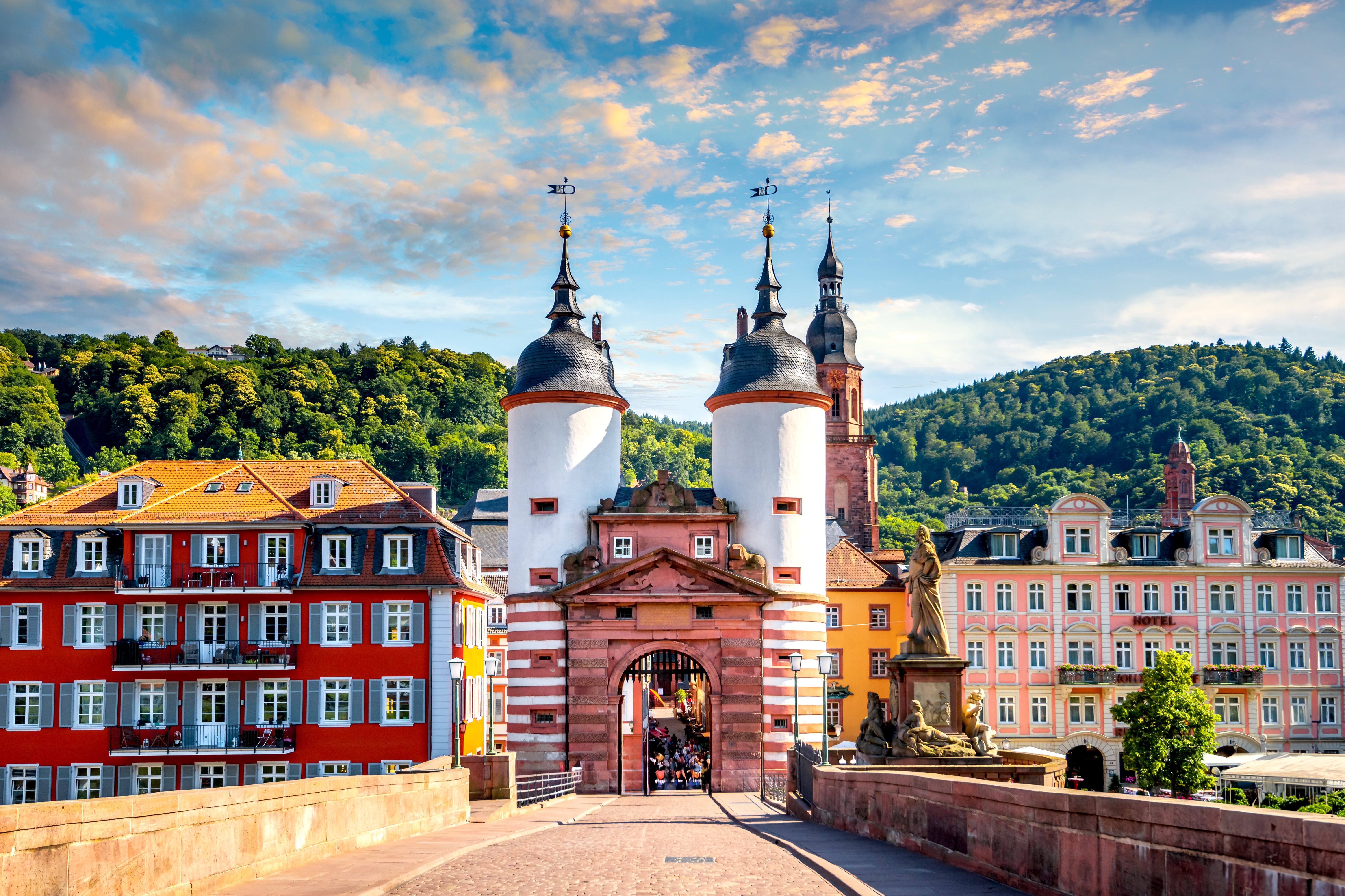 Idyllisk udsigt over den historiske broport i Heidelberg med hvide tårne og rød sandsten, omgivet af farverige bygninger og skovklædte bakker i Tyskland