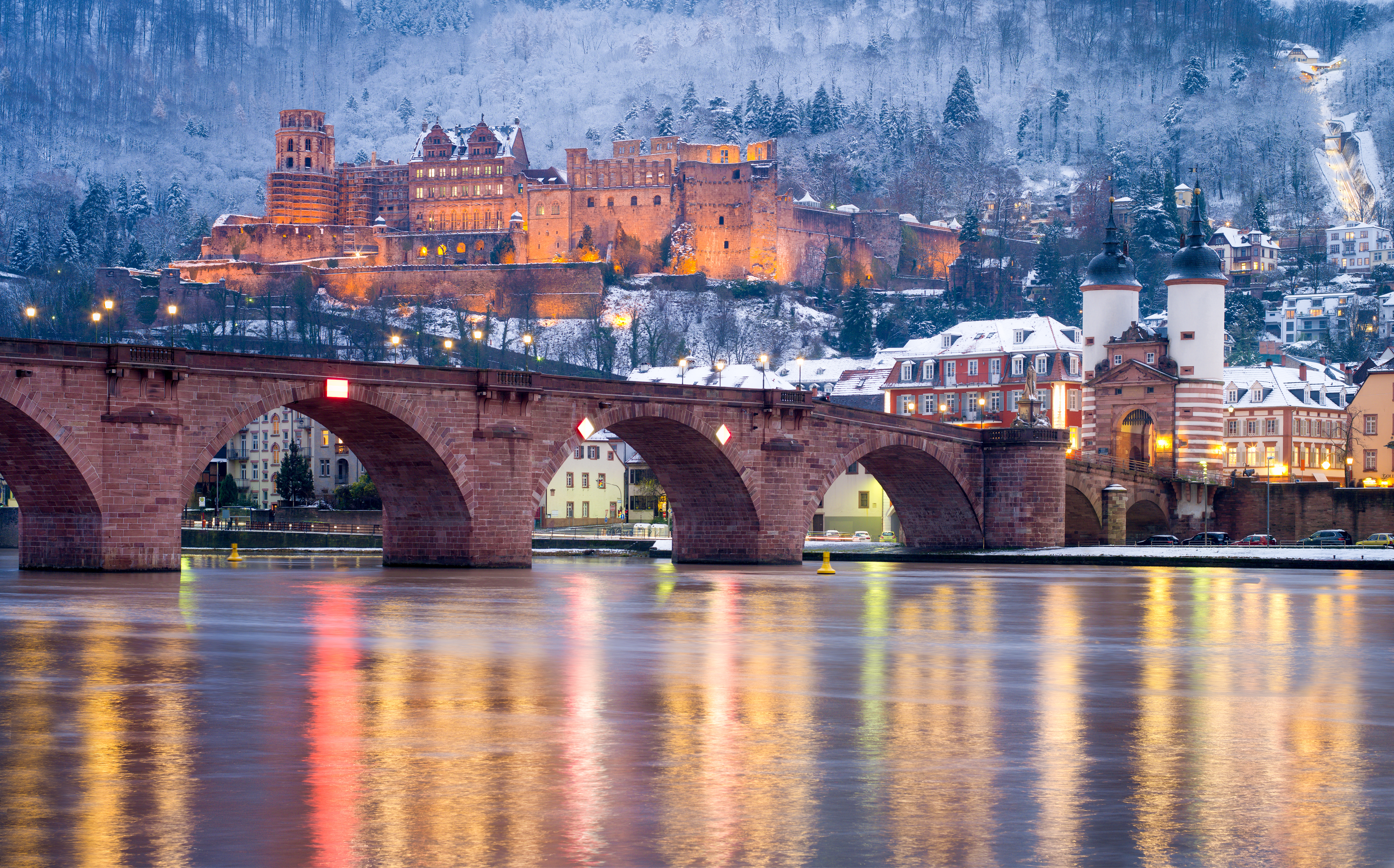 Eventyrlig udsigt over Heidelbergs gamle by med det oplyste middelalderslot og den historiske bro reflekteret i Neckar-floden på en smuk vinteraften