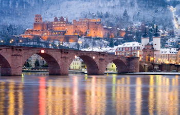 Eventyrlig udsigt over Heidelbergs gamle by med det oplyste middelalderslot og den historiske bro reflekteret i Neckar-floden på en smuk vinteraften