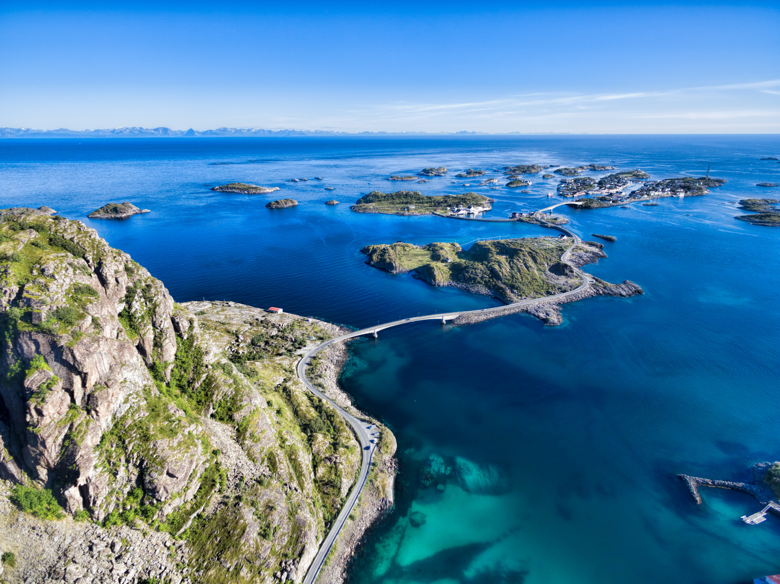 Smukt luftfoto af Henningsvær på Lofoten-øerne i Norge med turkisblåt hav, klippeøer og broer der forbinder den pittoreske fiskerby