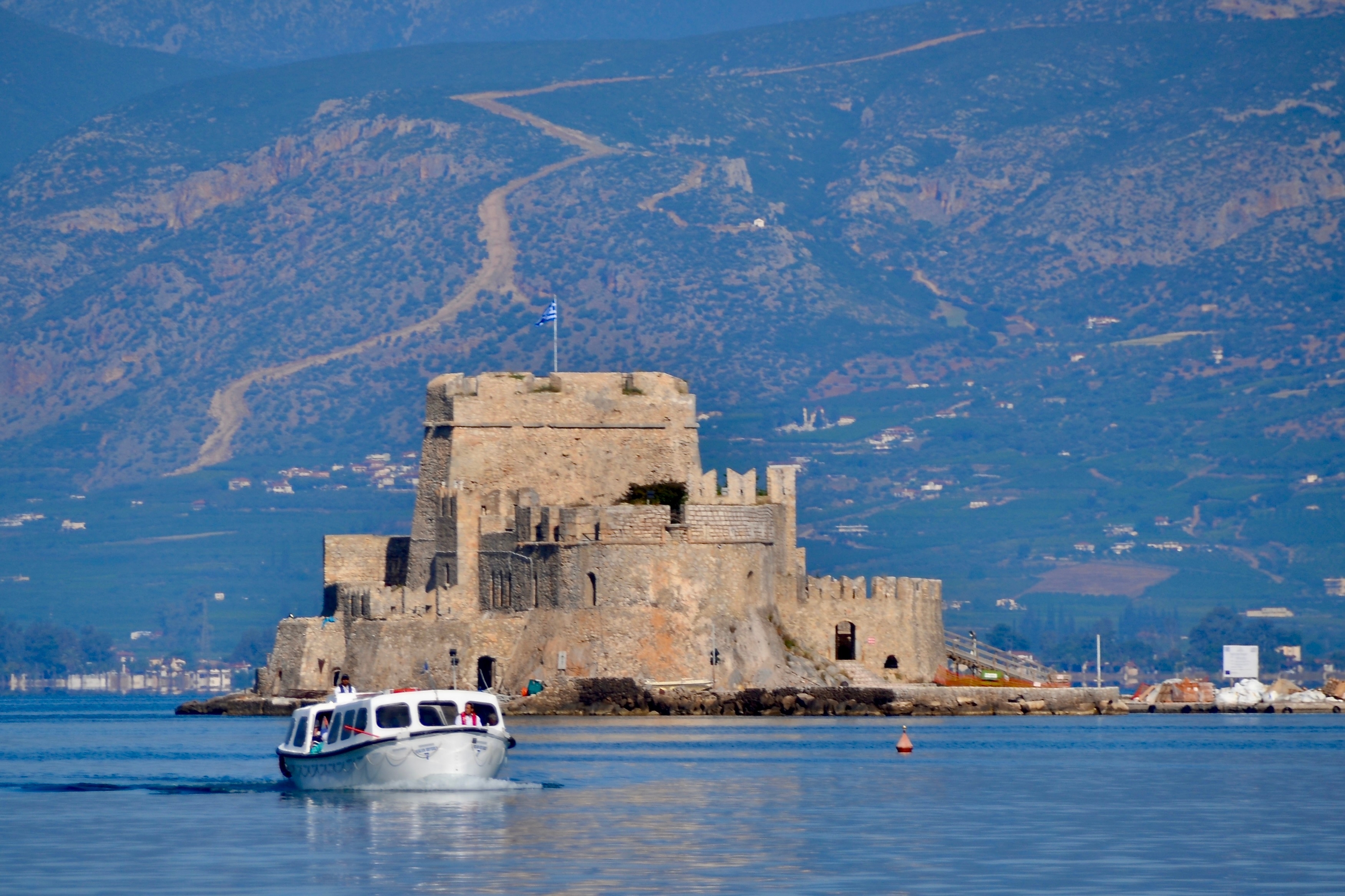 Historisk fæstning på ø ved Nafplio havn i Grækenland med traditionel båd