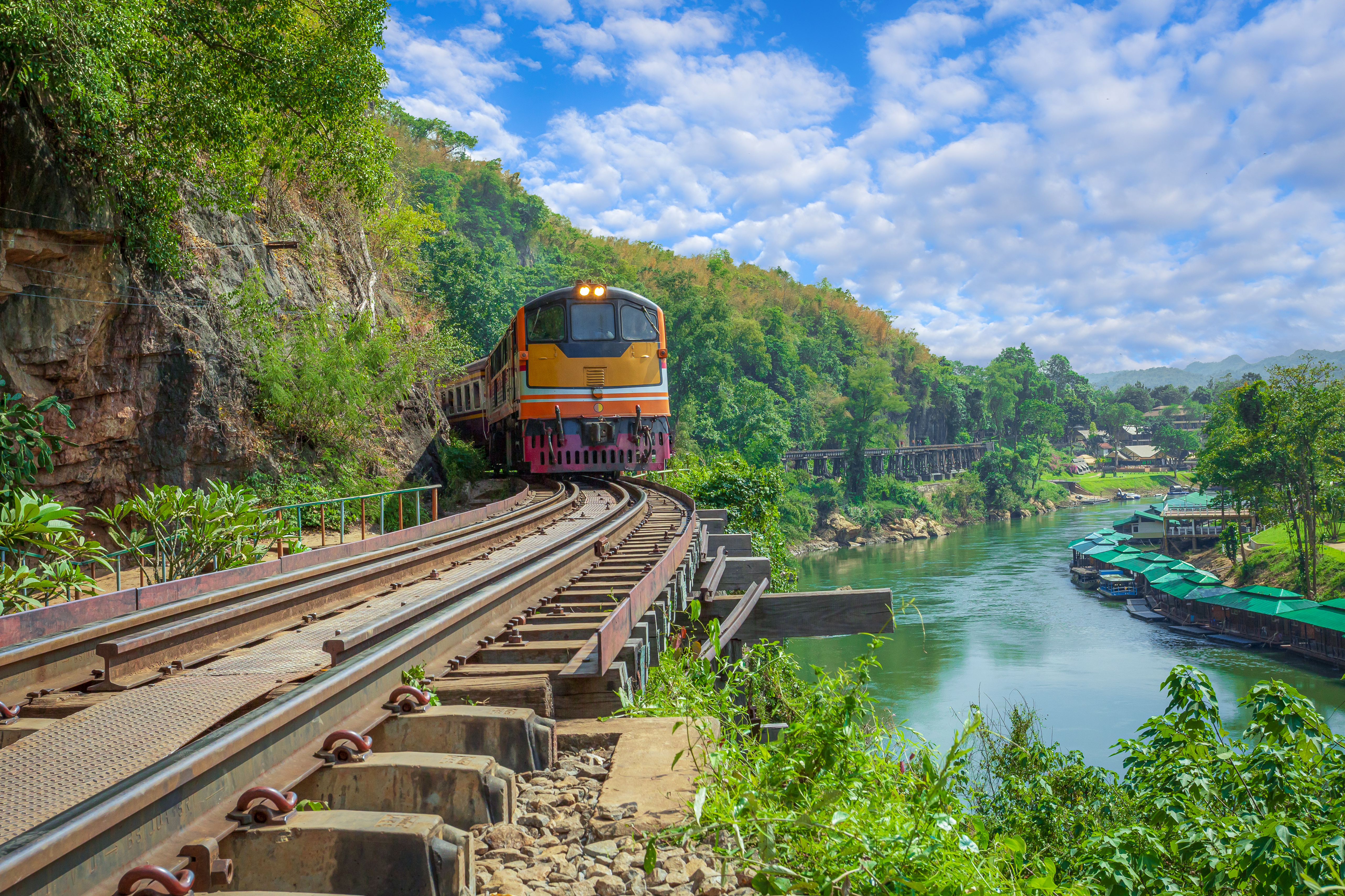 Tog på den historiske jernbanebro over River Kwai i Kanchanaburi Thailand omgivet af grøn jungle