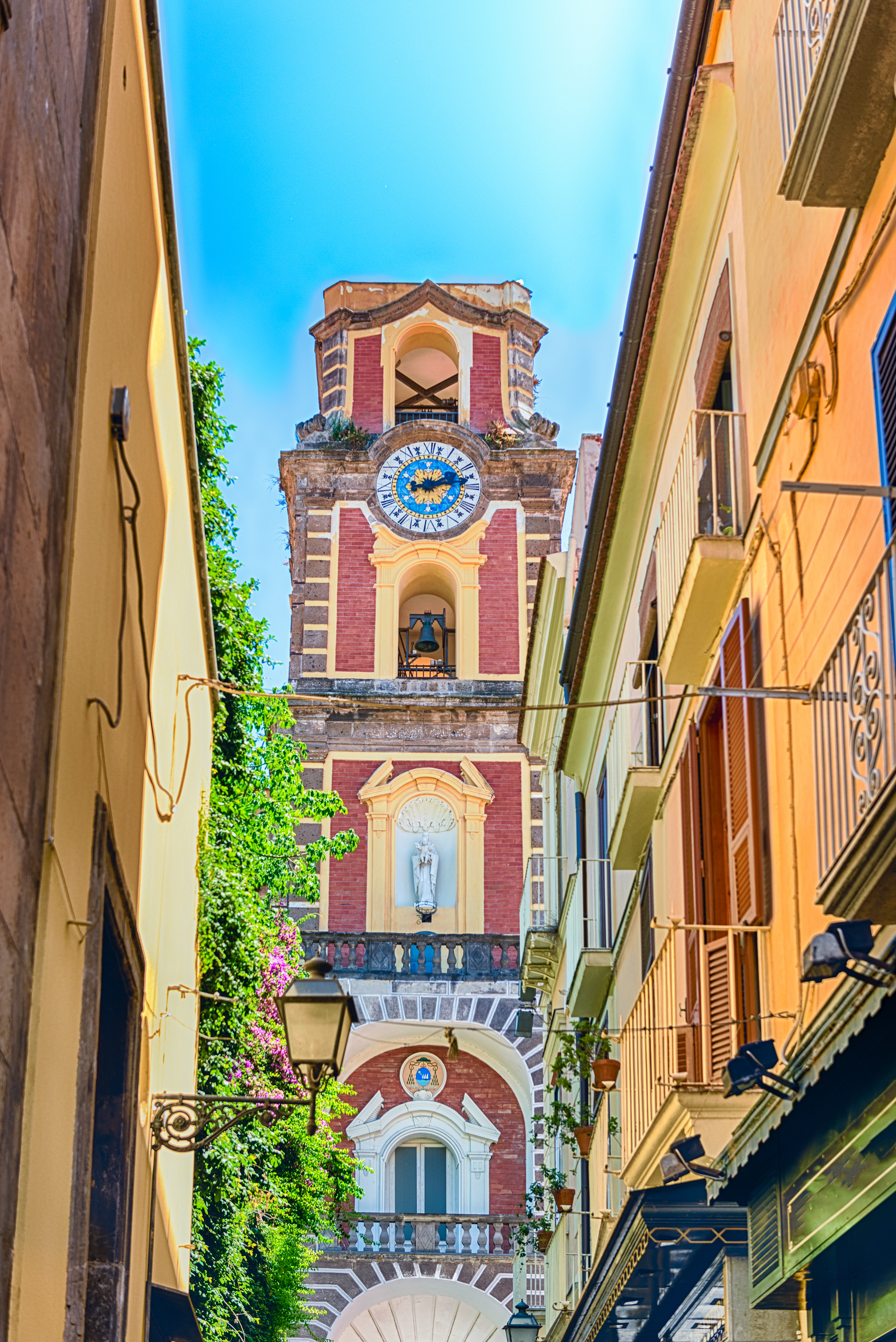 Imponerende klokketårn med detaljer set mellem bygninger i Sorrento Italien