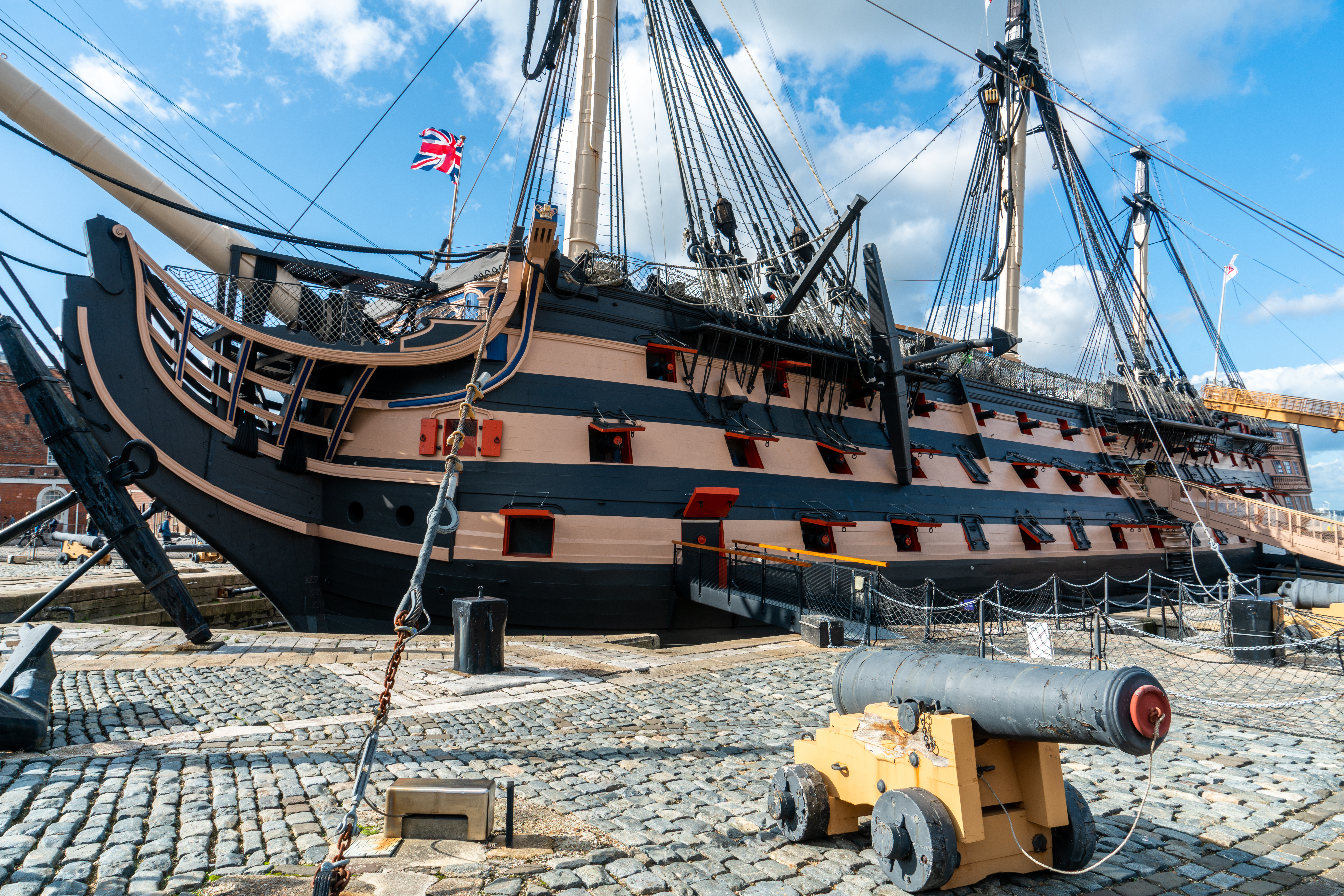 Det ikoniske britiske krigsskib HMS Victory fortøjet ved Portsmouth Historic Dockyard med Union Jack vajende fra masten og en gammel kanon i forgrunden