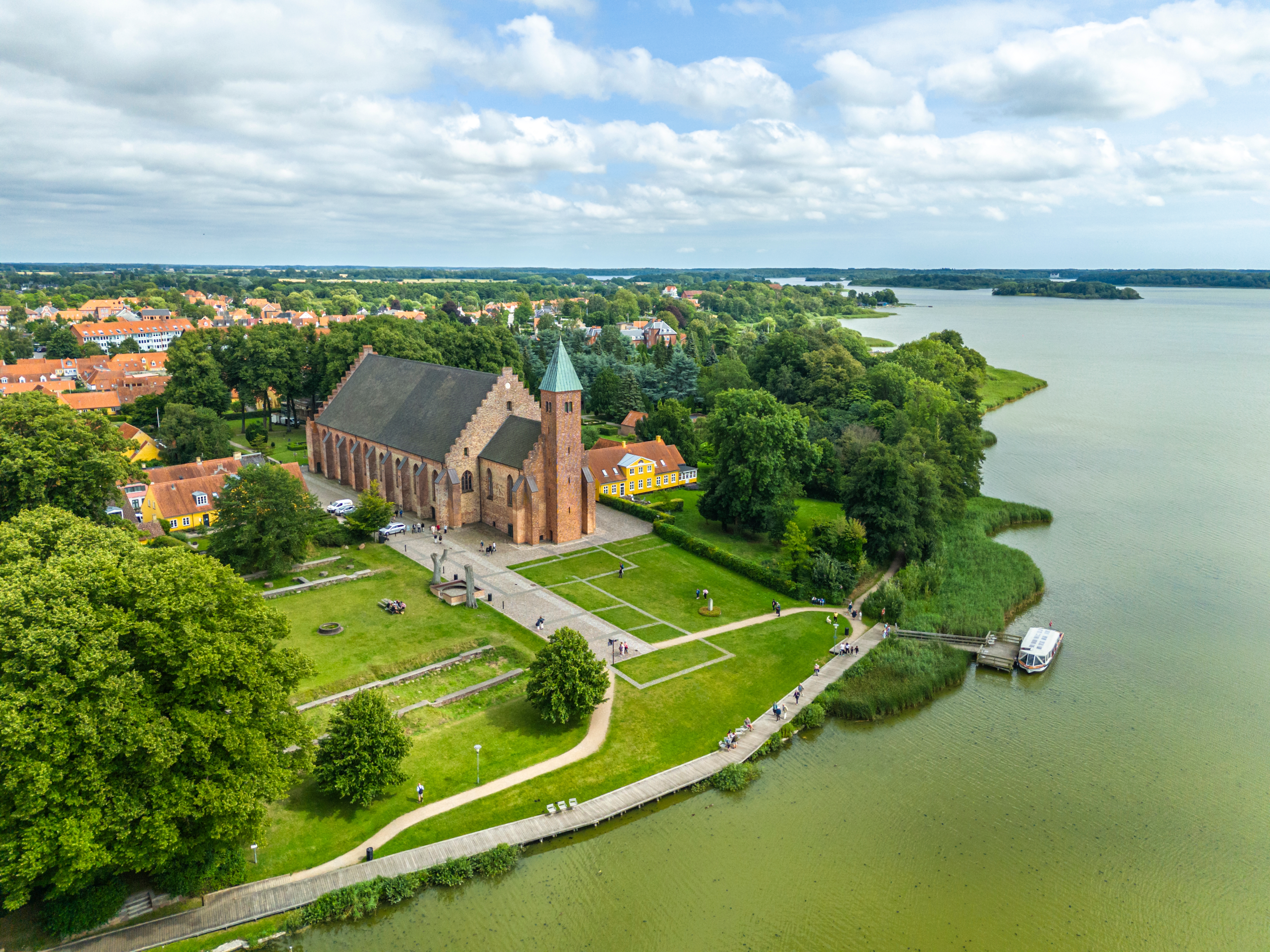 Historisk Maribo Kirke set fra luften med teglstensfacade, sø og frodig grøn natur i baggrunden