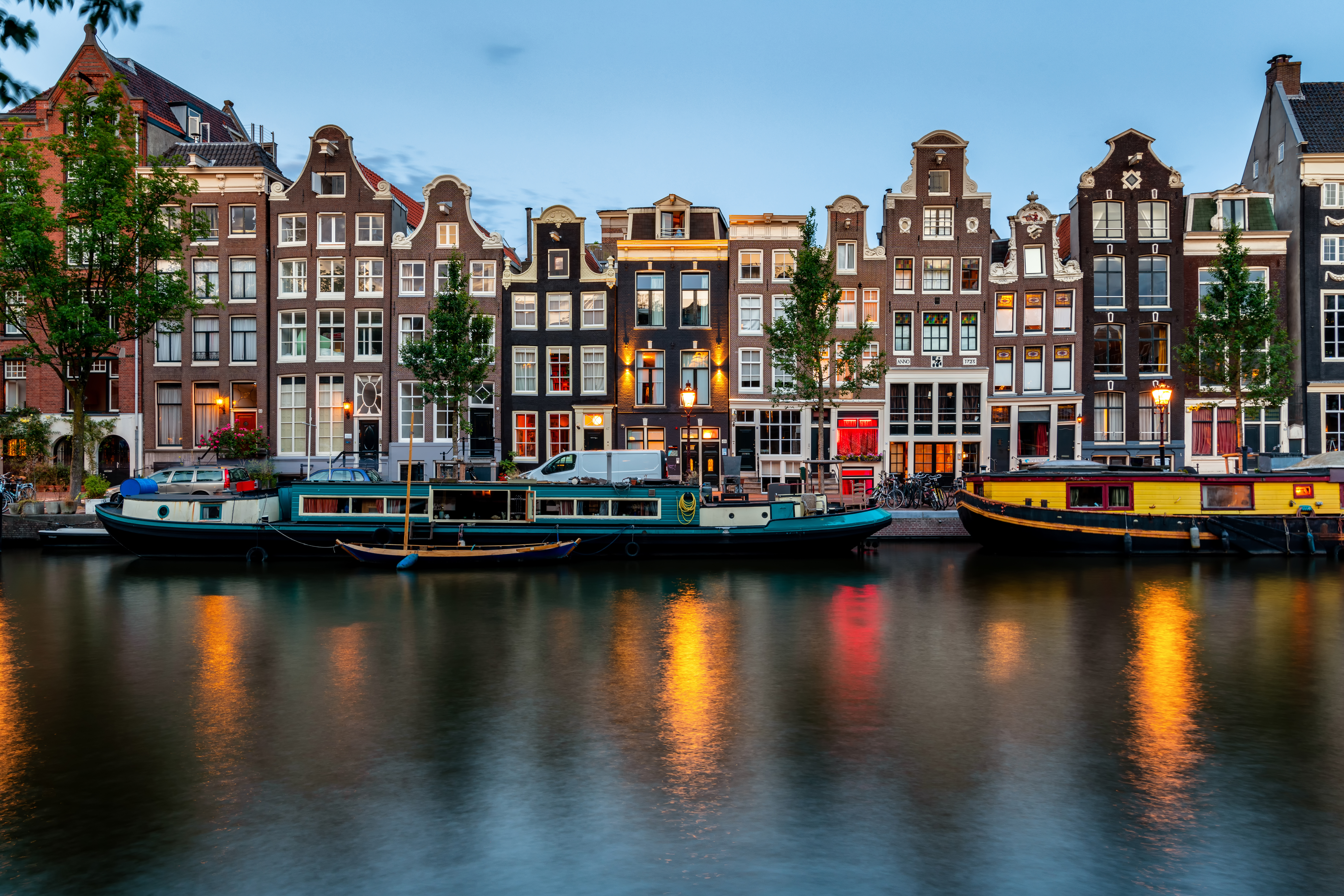 Farverige kanalhuse i Amsterdam med lys der spejler sig i vandet