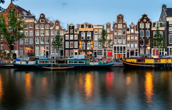 Farverige kanalhuse i Amsterdam med lys der spejler sig i vandet