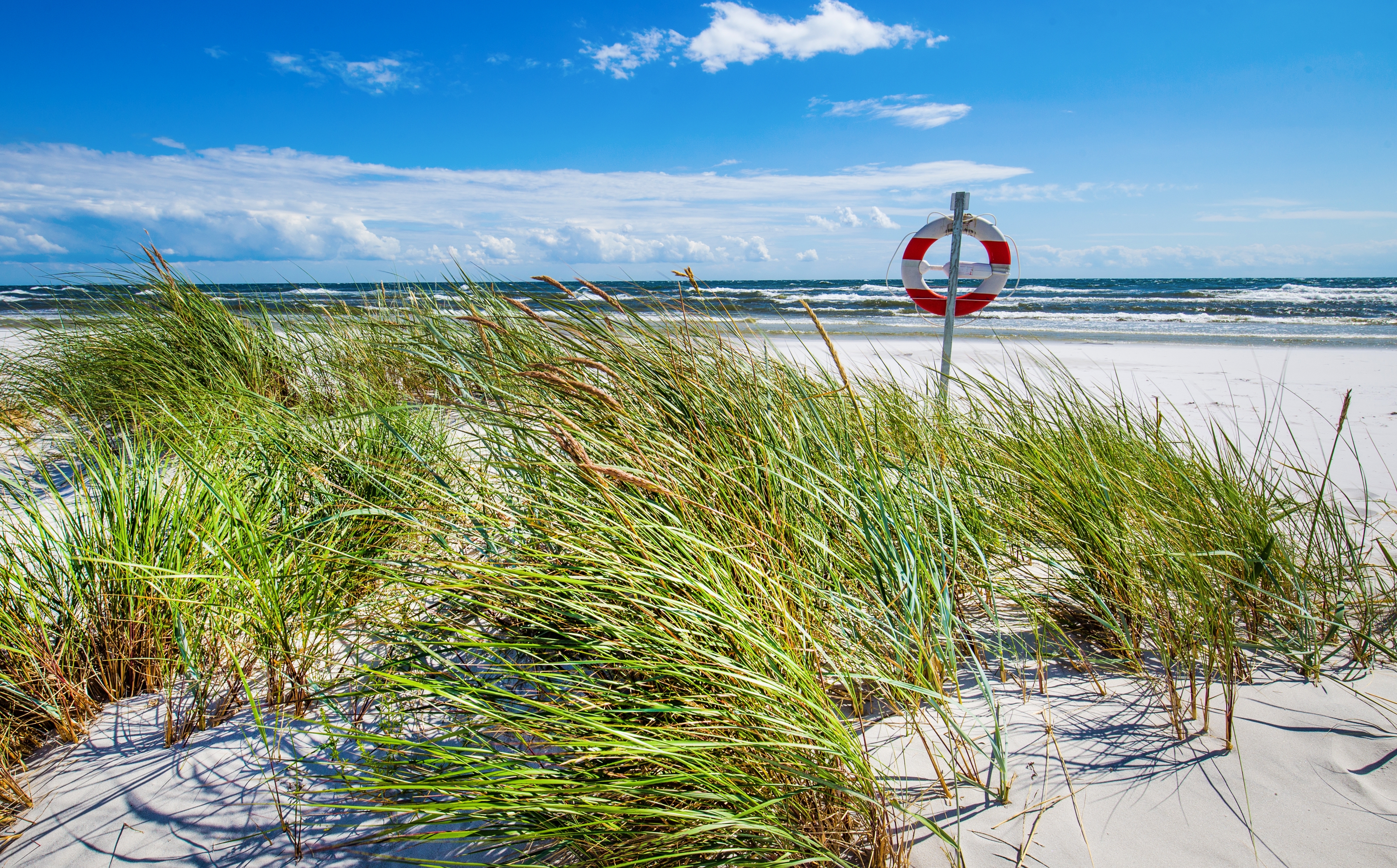 Naturskønt strandlandskab ved Dueodde på Bornholm med karakteristiske hvide sandklitter og det klare blå hav, der skaber perfekte rammer for en dansk badeferie