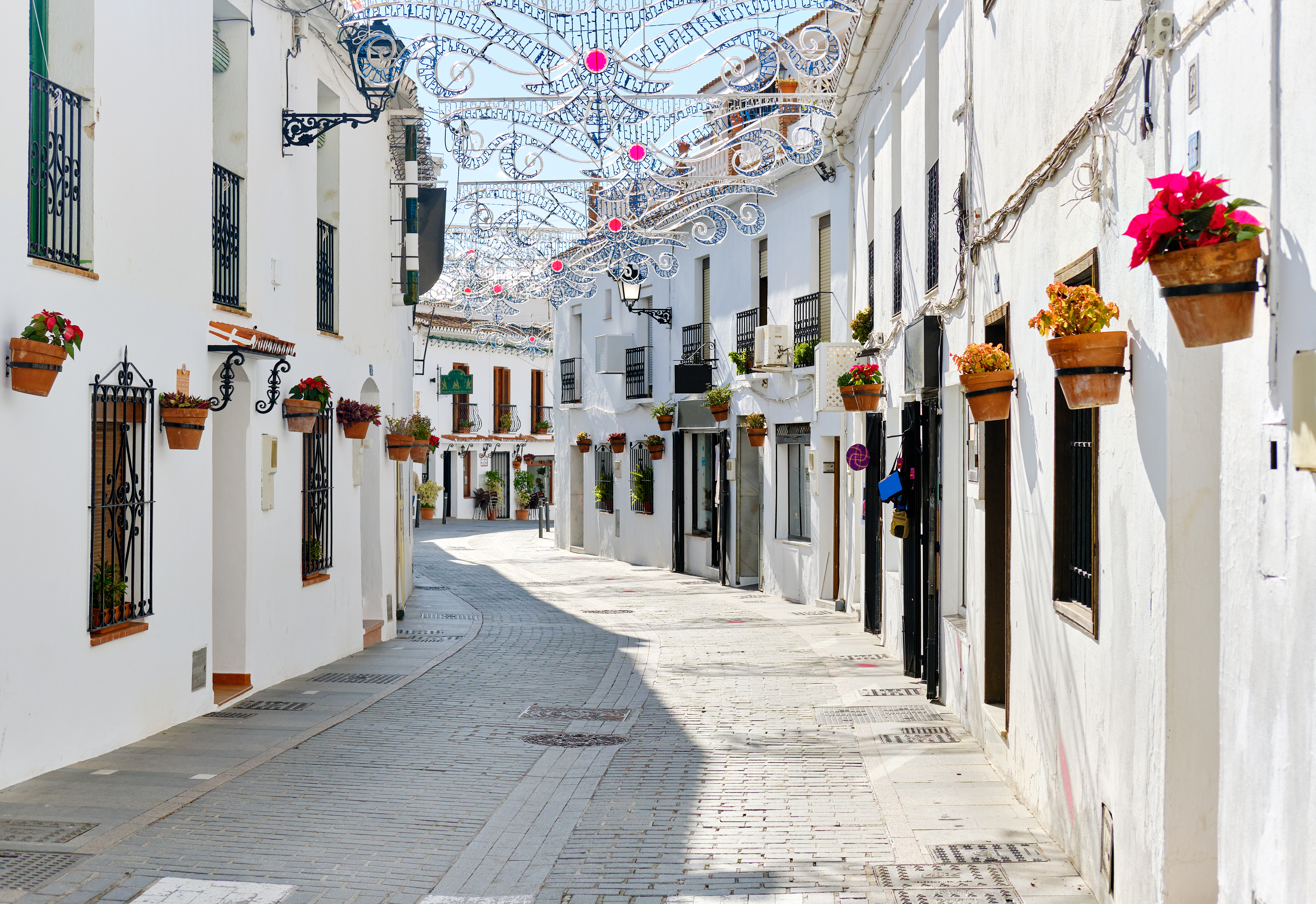 Rolig og solrig gade i det hvidkalkede Mijas på Costa del Sol i Spanien med blomsterkrukker på væggene og festlige dekorationer