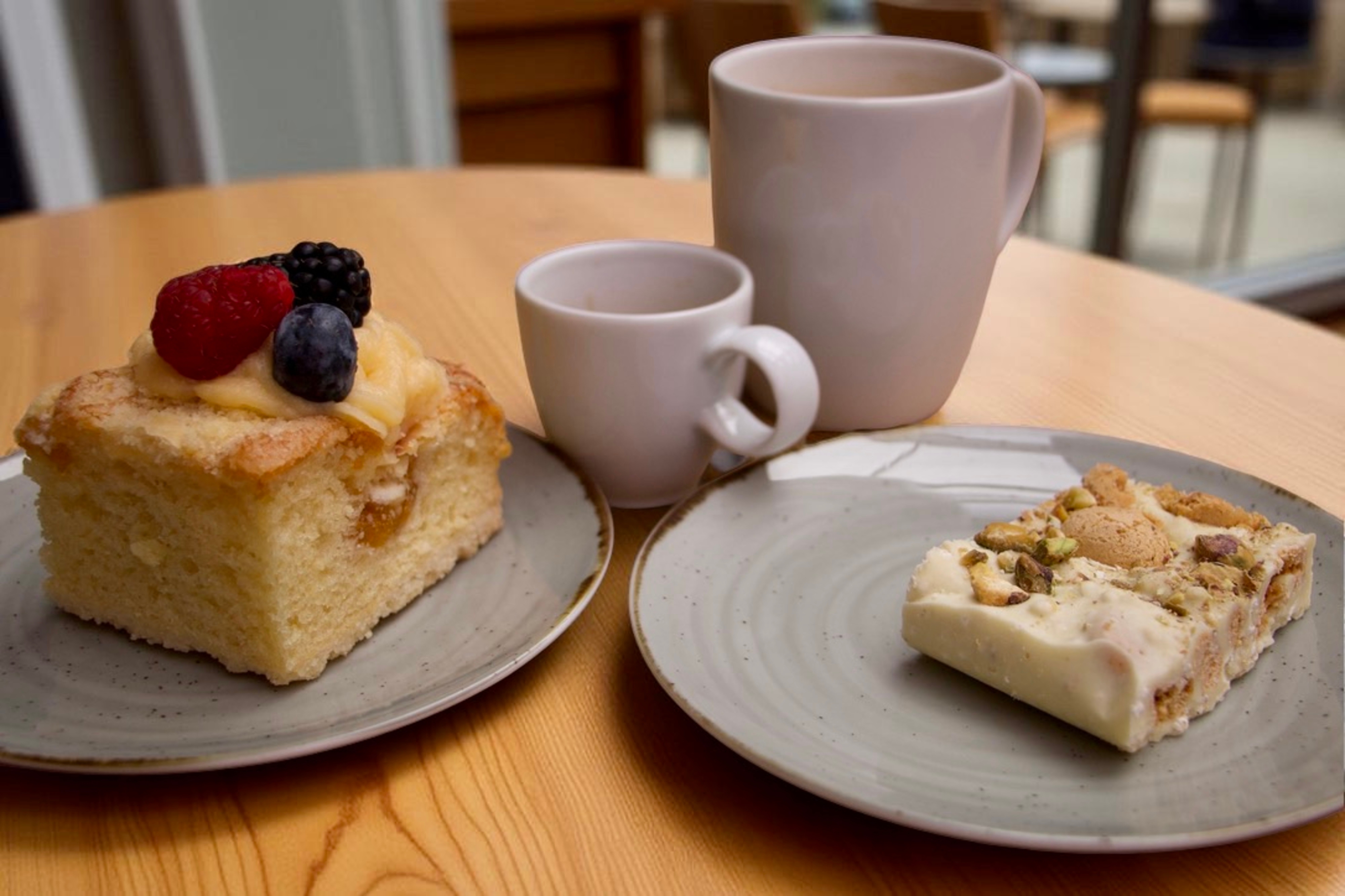 Indbydende kagebord på britisk café med saftig vaniljekage toppet med friske bær og en skive hvid chokoladekage med pistacienødder og kaffe