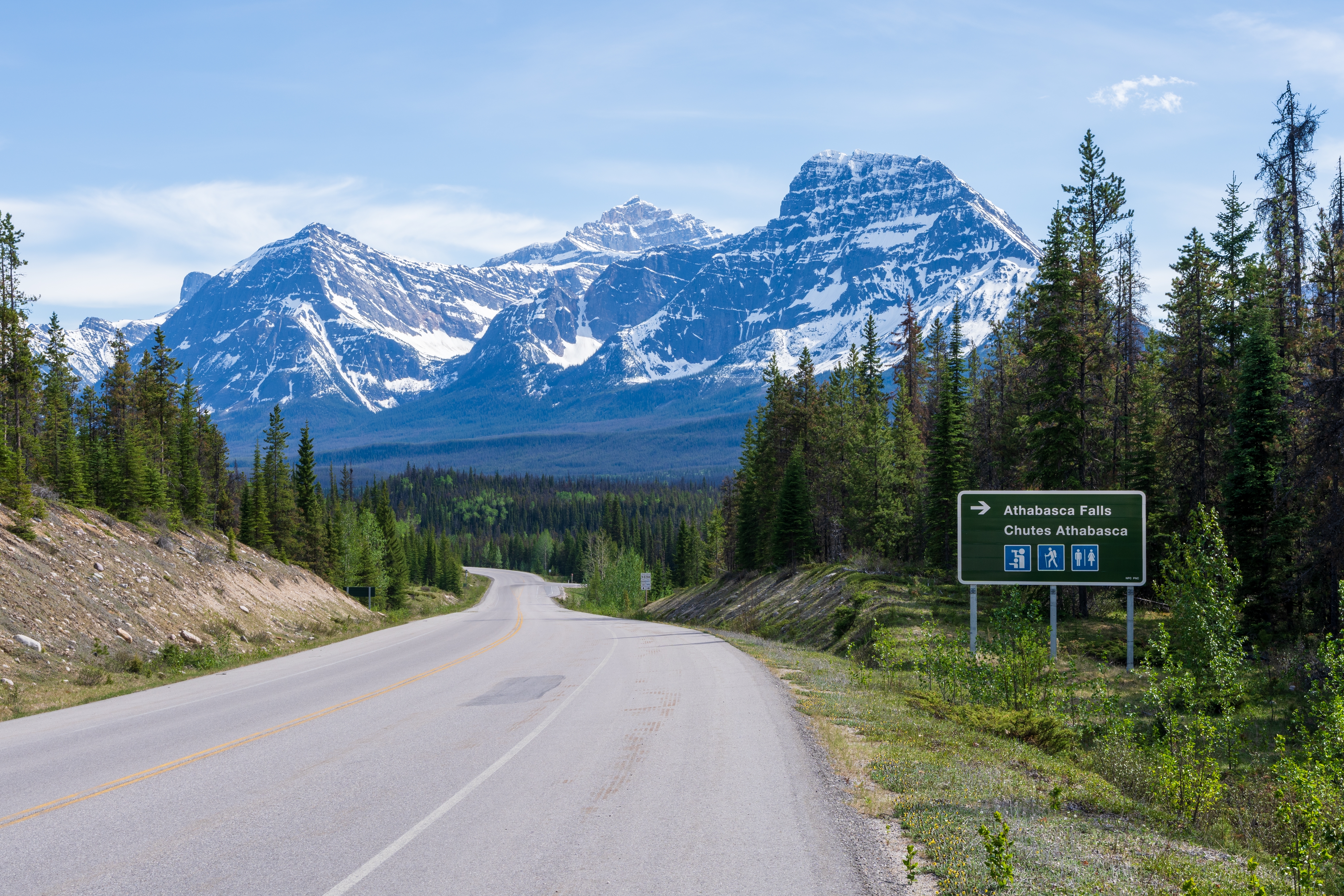 Vejskilt der viser vej til Athabasca Falls på den berømte Icefields Parkway i Jasper National Park, med dramatiske snedækkede bjergtinder og grønne nåleskove i Canada