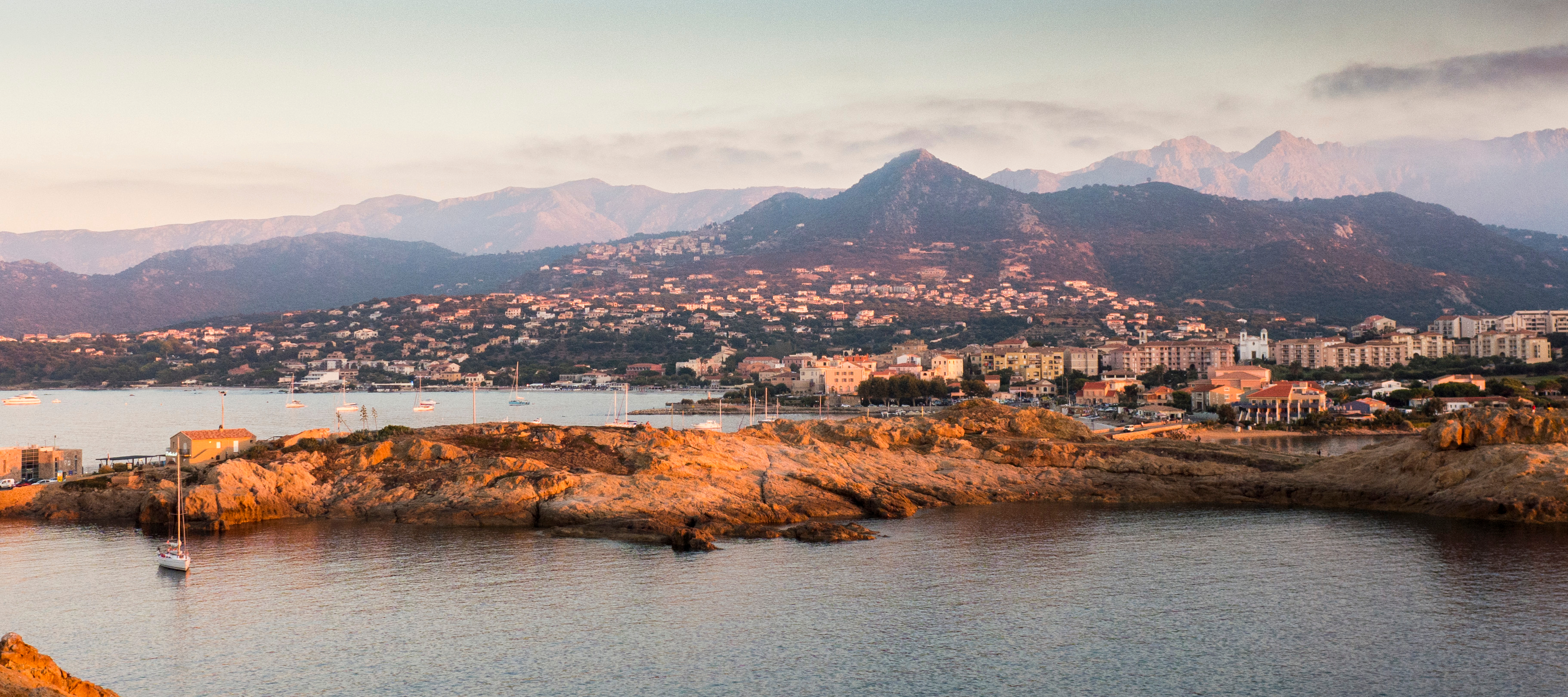 Magisk solnedgangsstemning ved L'Île-Rousse havn på Korsika med gyldne klippekyst og fredelige middelhavsvande
