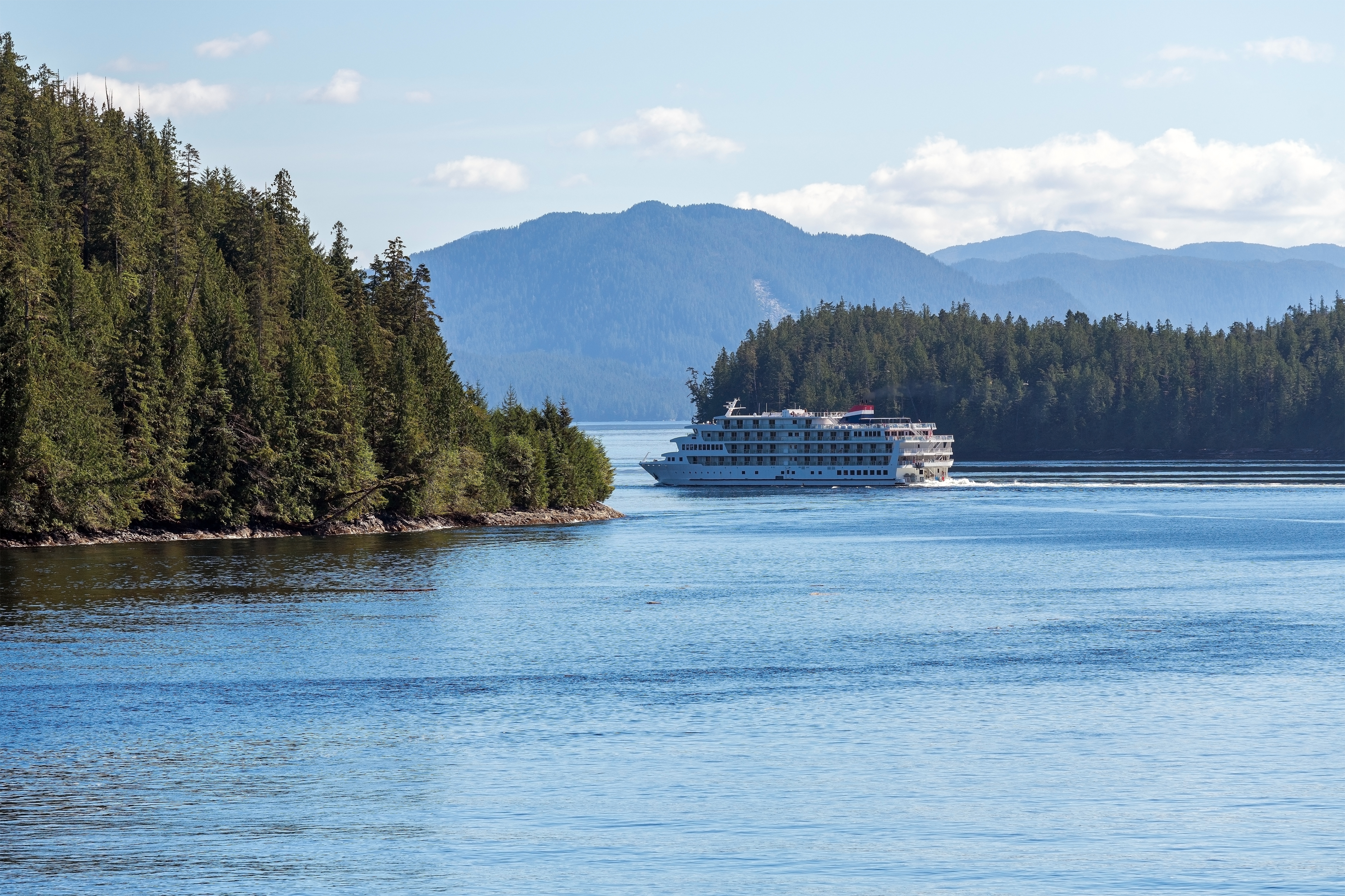 Krydstogtskib i den smukke Inside Passage ved Vancouver Island omgivet af frodig nåleskov og blå bjerge i British Columbia, Canada