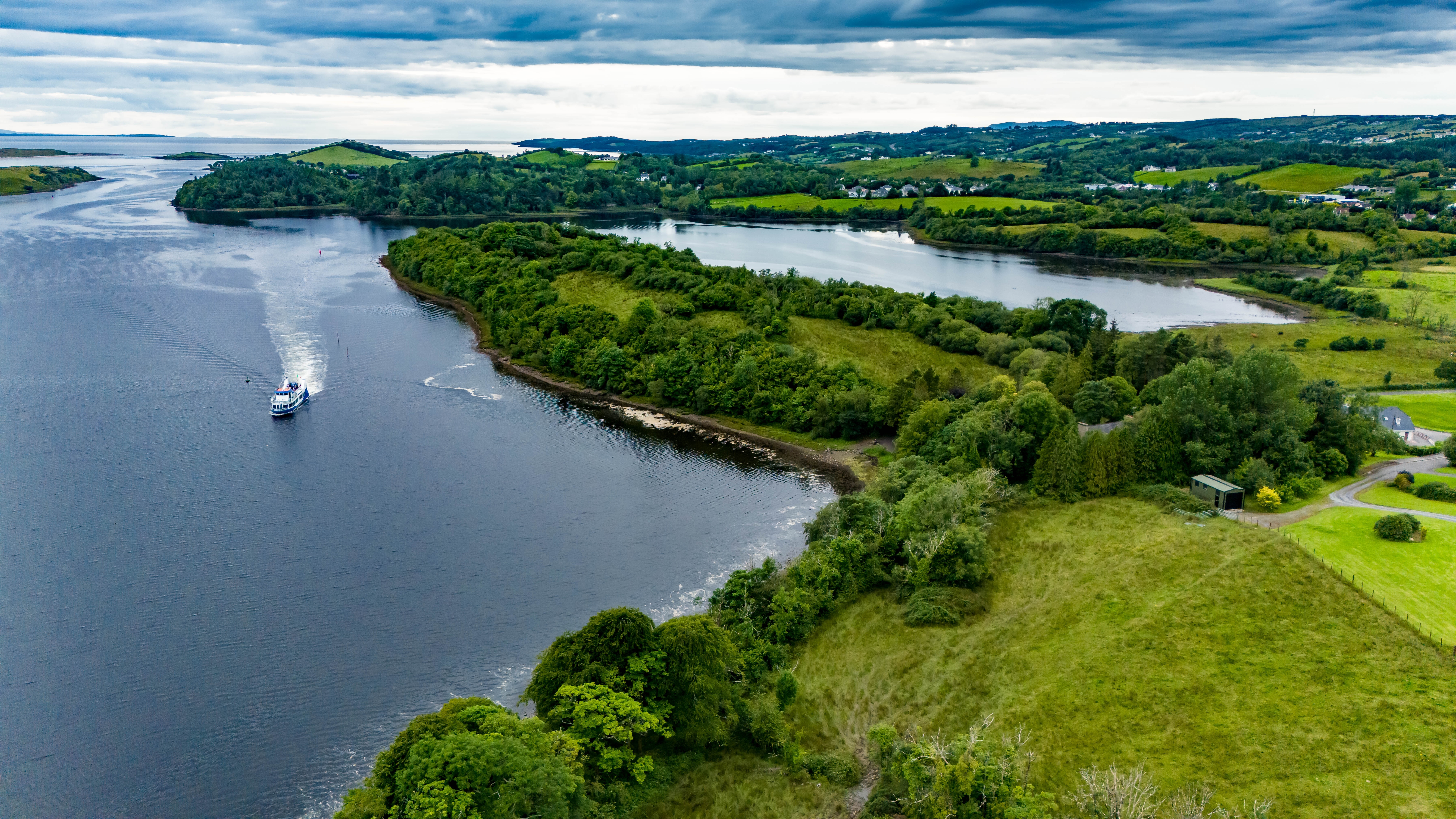 Naturskøn luftudsigt over den irske kystlinje ved Donegal med frodig grøn vegetation og en vandbus på det rolige vand