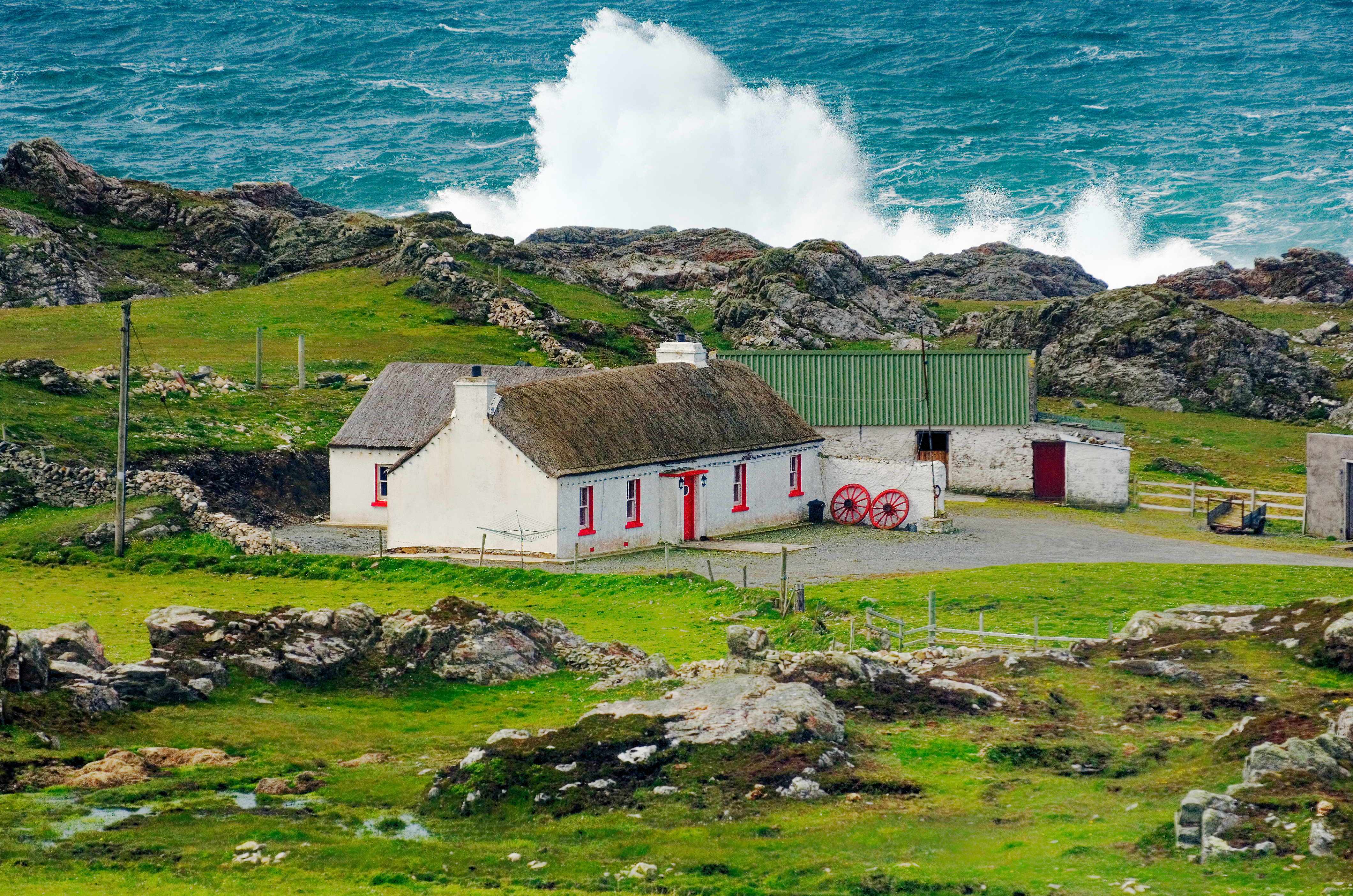 Idyllisk traditionelt stråtækt hus på Inishowen-halvøen ved Malin Head i County Donegal, Irland, med vilde atlantiske stormebølger der bryder mod den klippede kystlinje