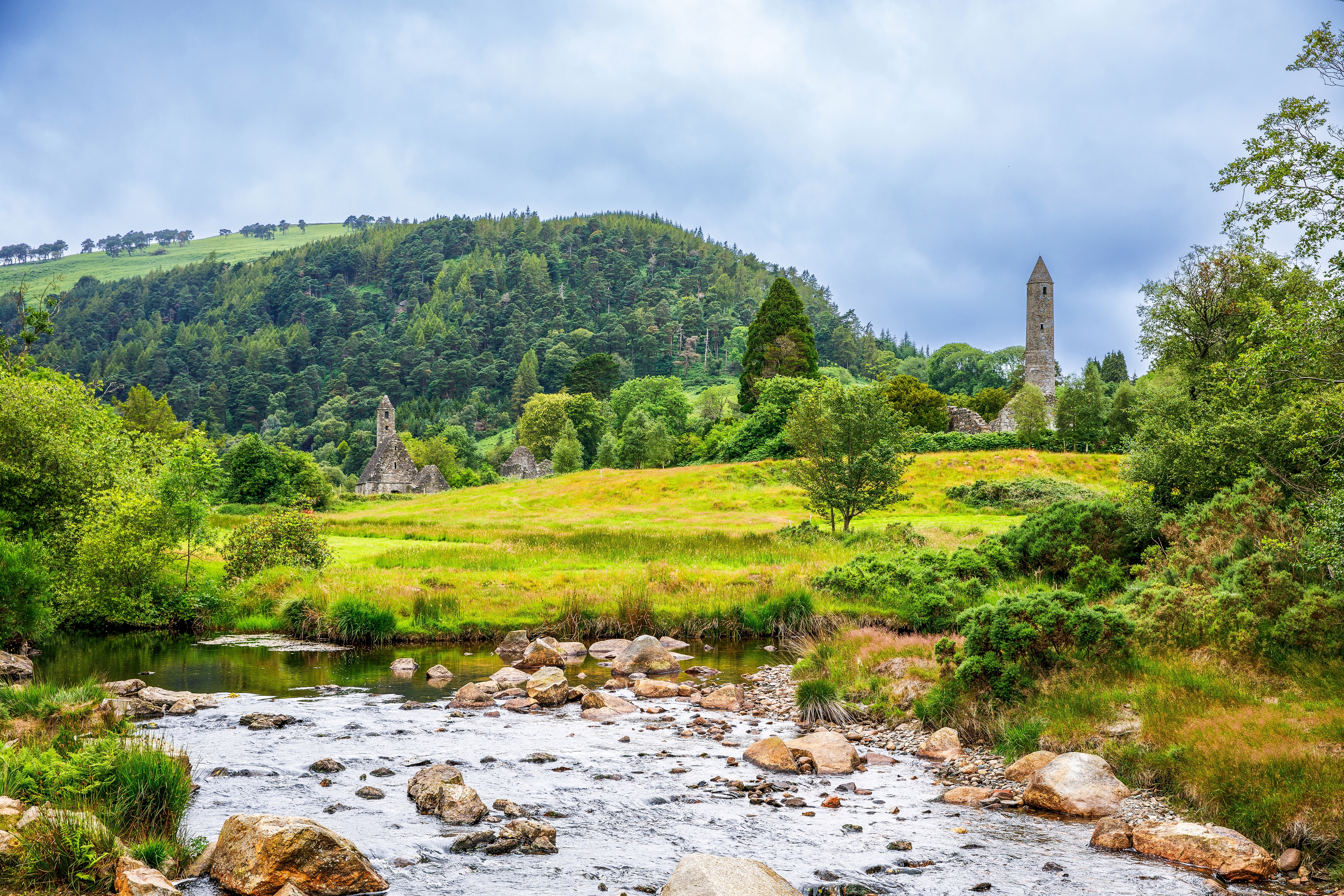 Middelalderligt rundtårn og klosterruiner ved floden i Glendalough, Irlands Wicklow County