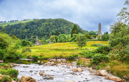 Middelalderligt rundtårn og klosterruiner ved floden i Glendalough, Irlands Wicklow County