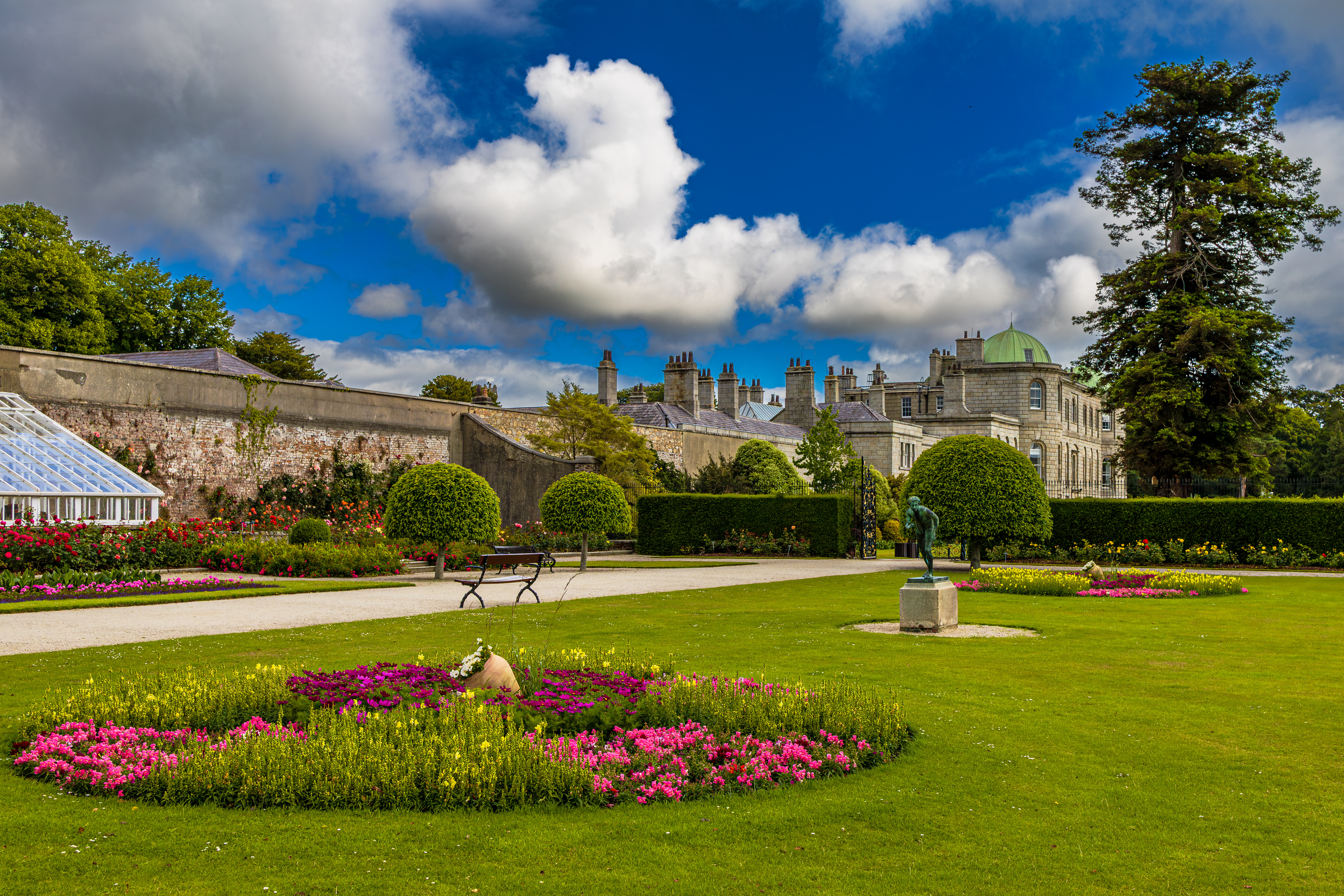 Historiske Powerscourt haver i County Wicklow, Irland, med farverige blomsterbede, symmetriske hække, bronzestatue og smuk georgisk herregård
