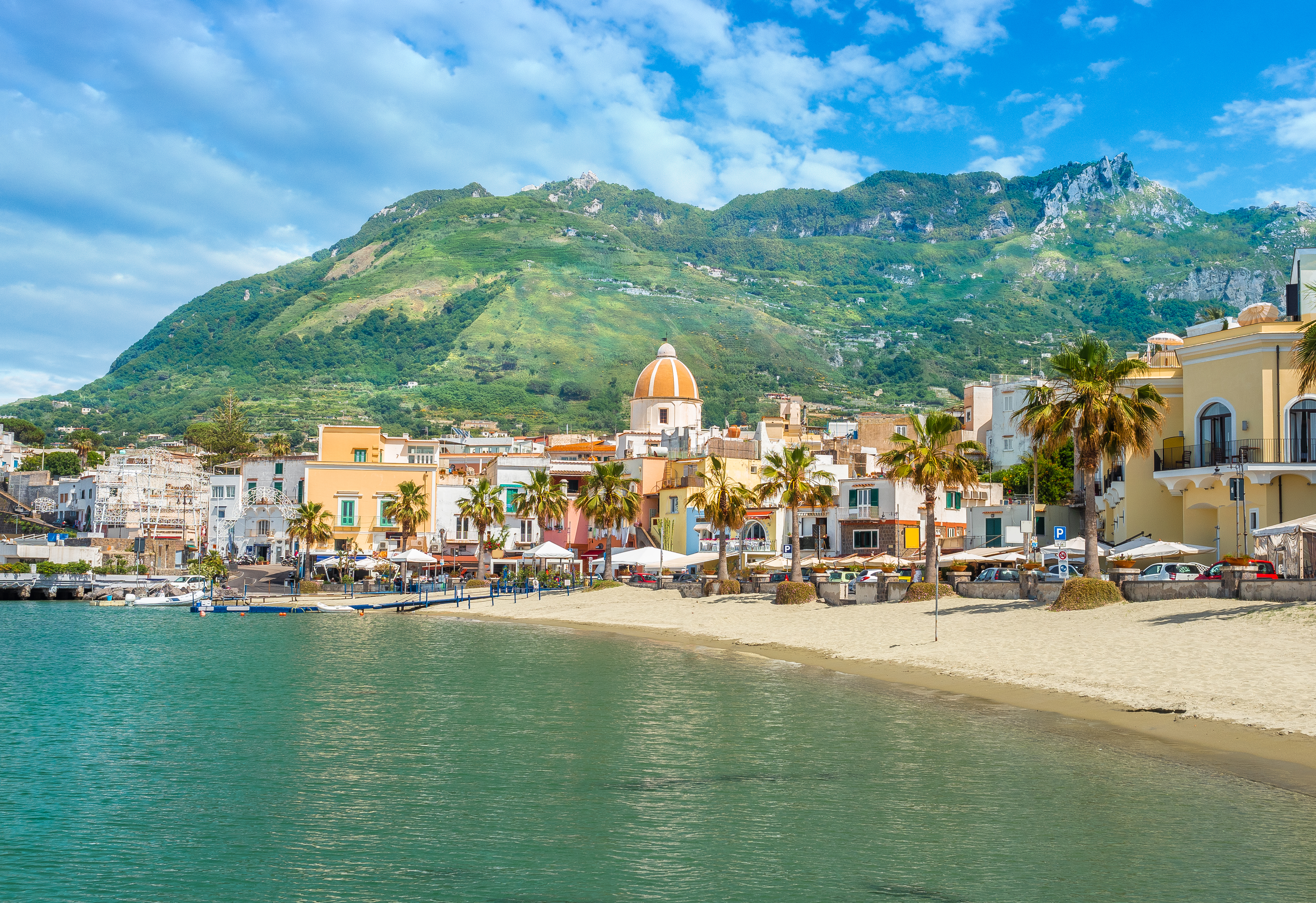 Smuk sandstrand i Forio på Ischia med farverige bygninger, palmer og grønne bjerge ved Middelhavet i Italien