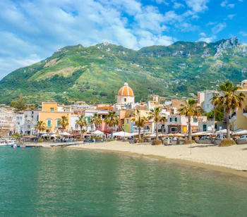 Smuk sandstrand i Forio på Ischia med farverige bygninger, palmer og grønne bjerge ved Middelhavet i Italien
