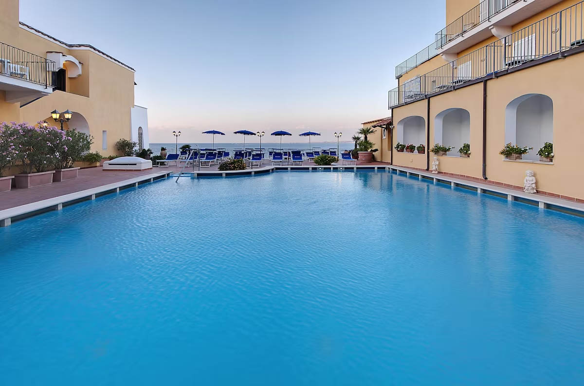 Indbydende hotelpool med udsigt over Middelhavet på øen Ischia, Italien, med blå parasoller og liggestole