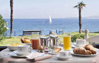 Feriemorgenmad med kaffe, juice og croissanter med udsigt til Middelhavet og en sejlbåd fra Ischia