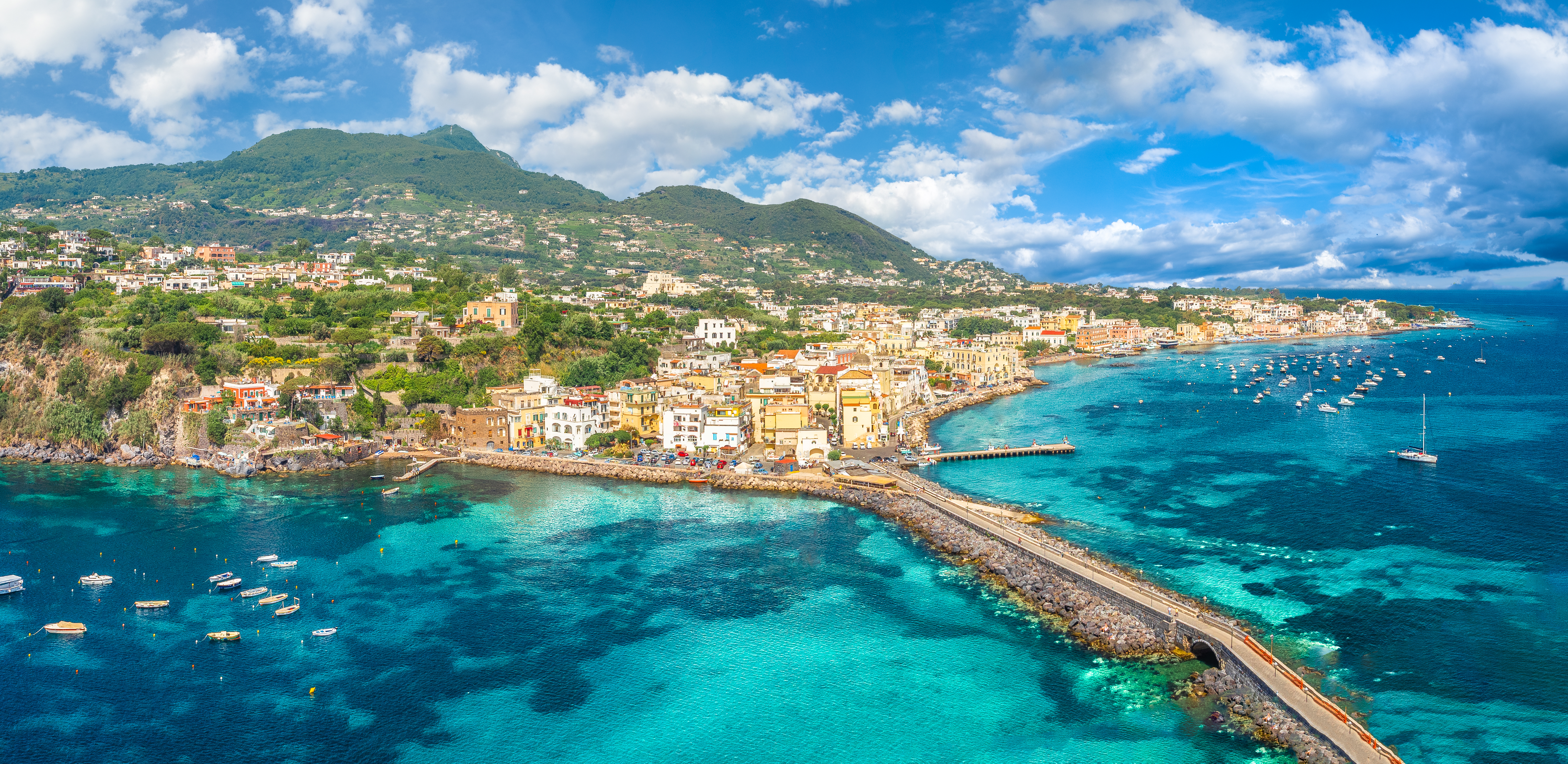 Skøn udsigt over Ischia Porto med det turkisblå Middelhav, farverige bygninger langs kysten og grønne bjerge bagved